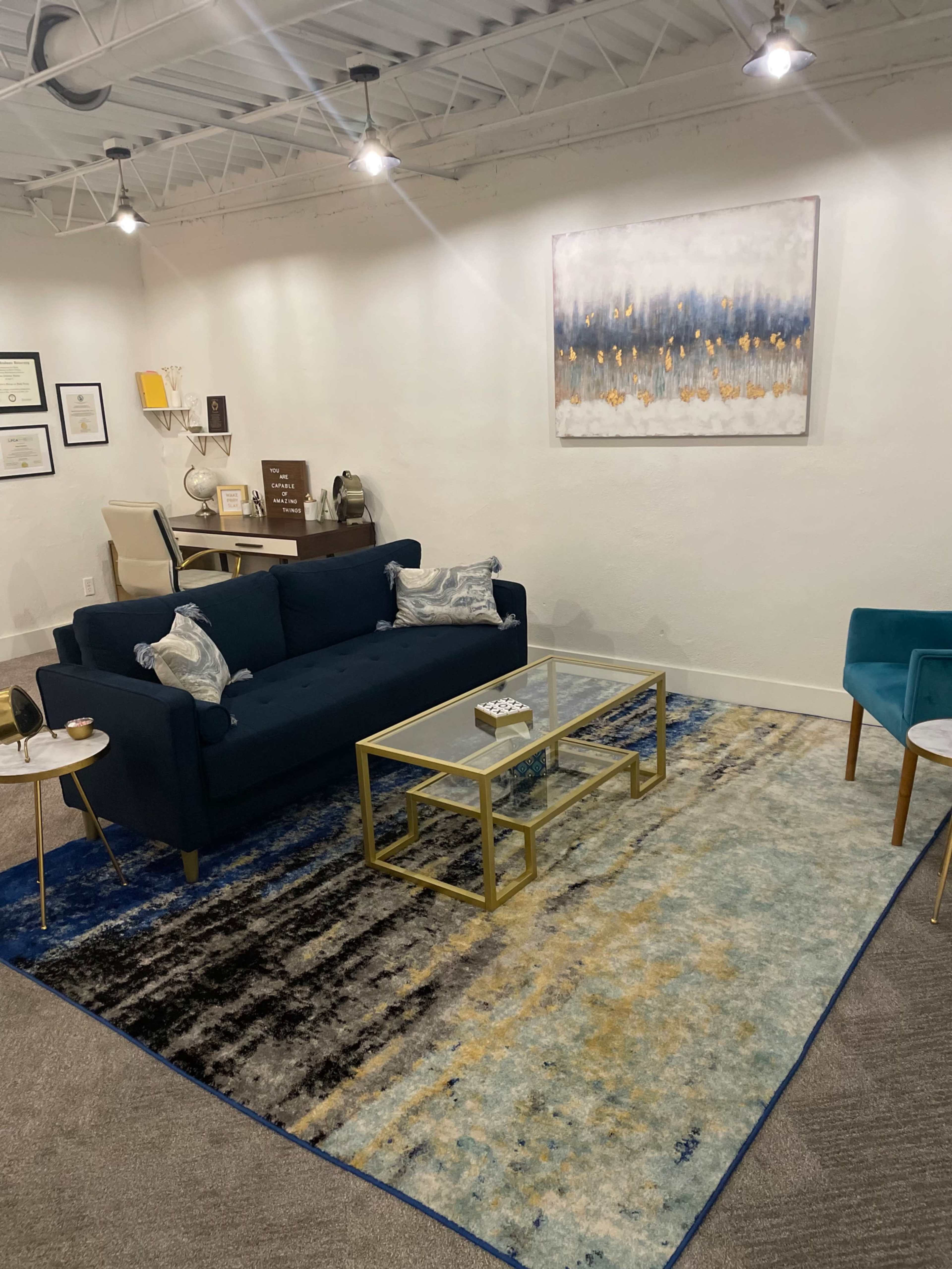 The image shows a modern office waiting area with a blue sofa, a glass coffee table, and a large area rug under soft lighting.