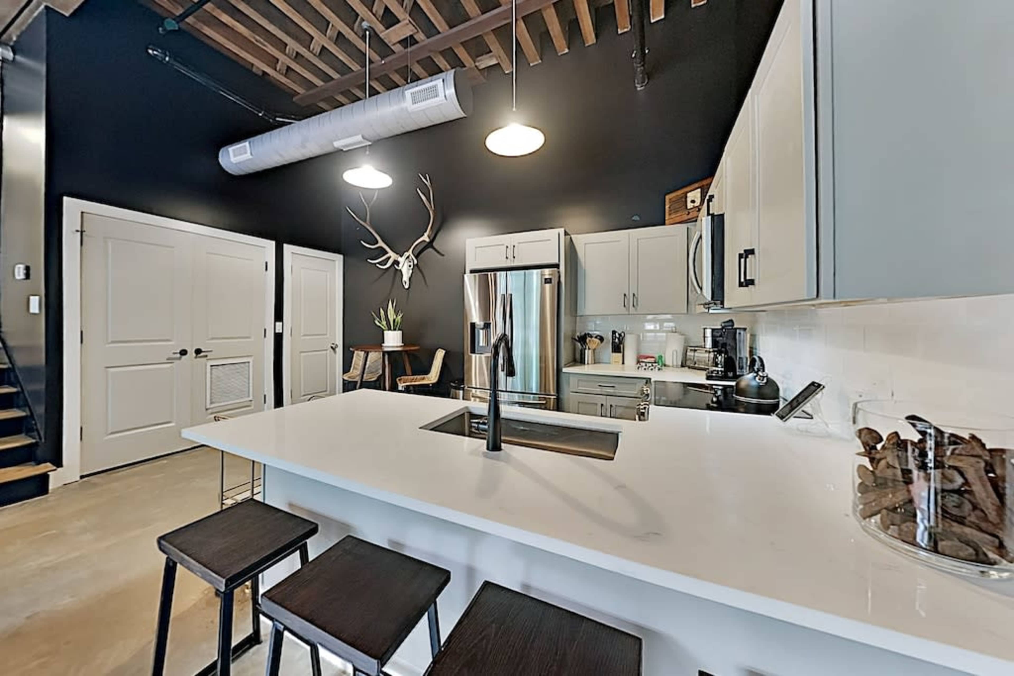 The image shows a modern kitchen with a large island, stainless steel appliances, and a black accent wall featuring deer antlers.