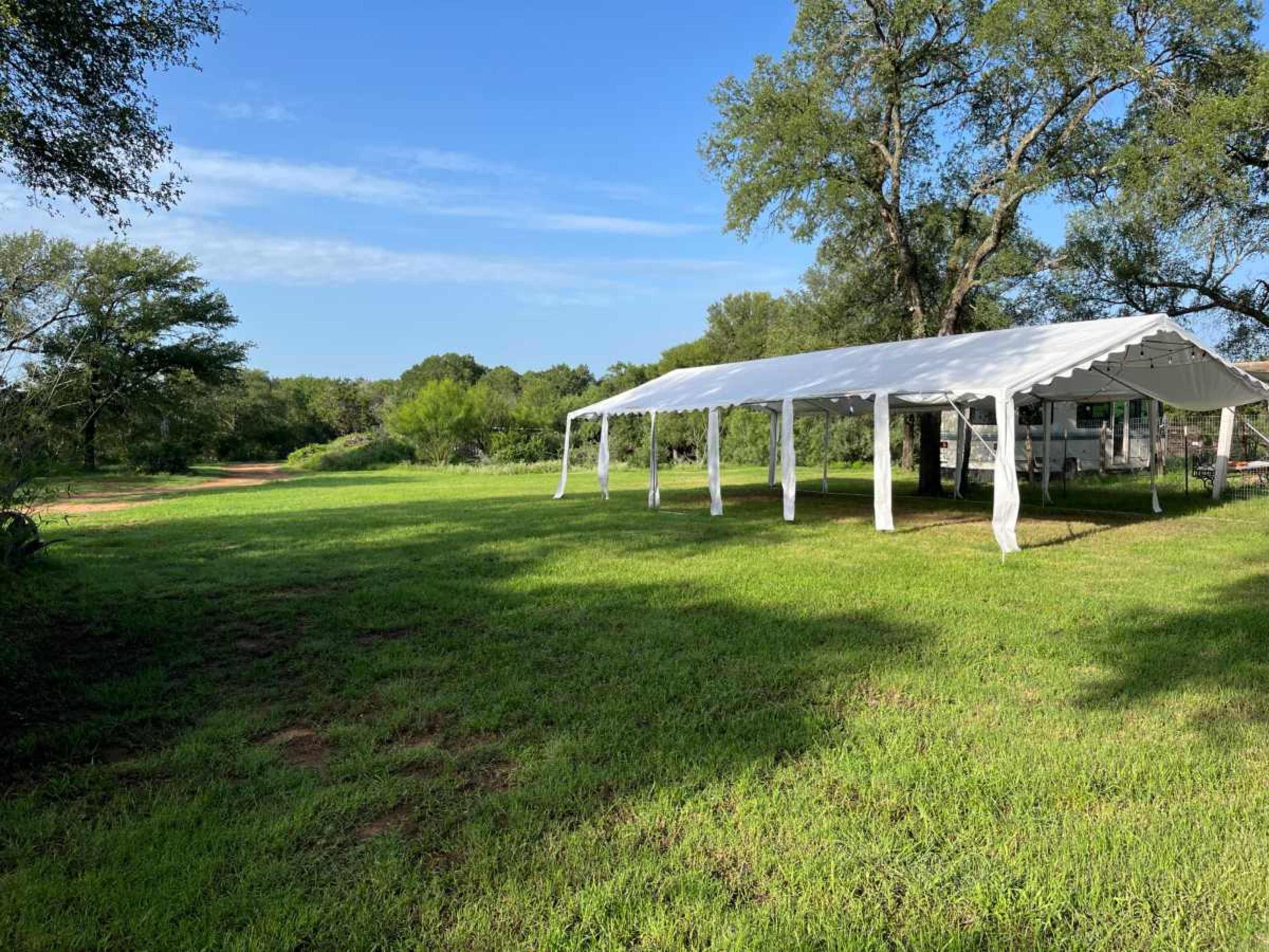 A white tent is set up on a grassy area surrounded by trees and open land.