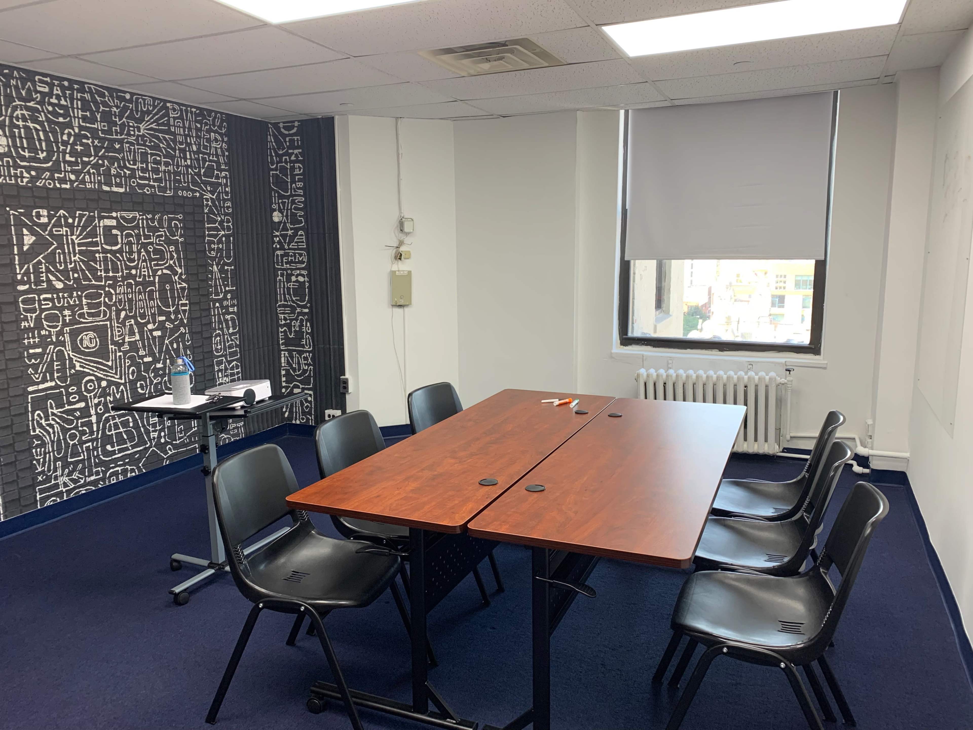 A meeting room with a large table surrounded by black chairs, a radiator, and a patterned wall design.