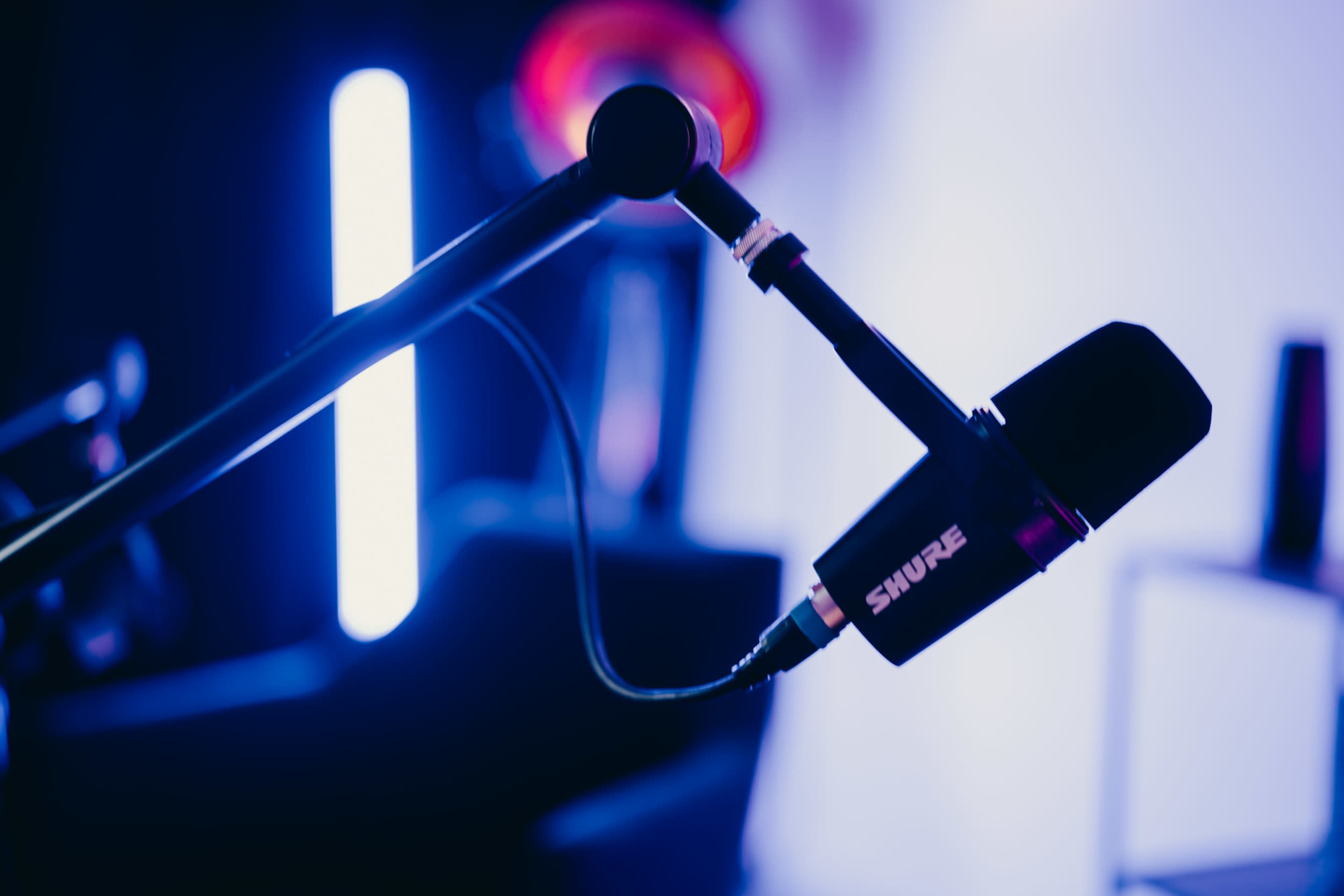 A Shure microphone is mounted on a microphone stand with colorful lighting in the background.