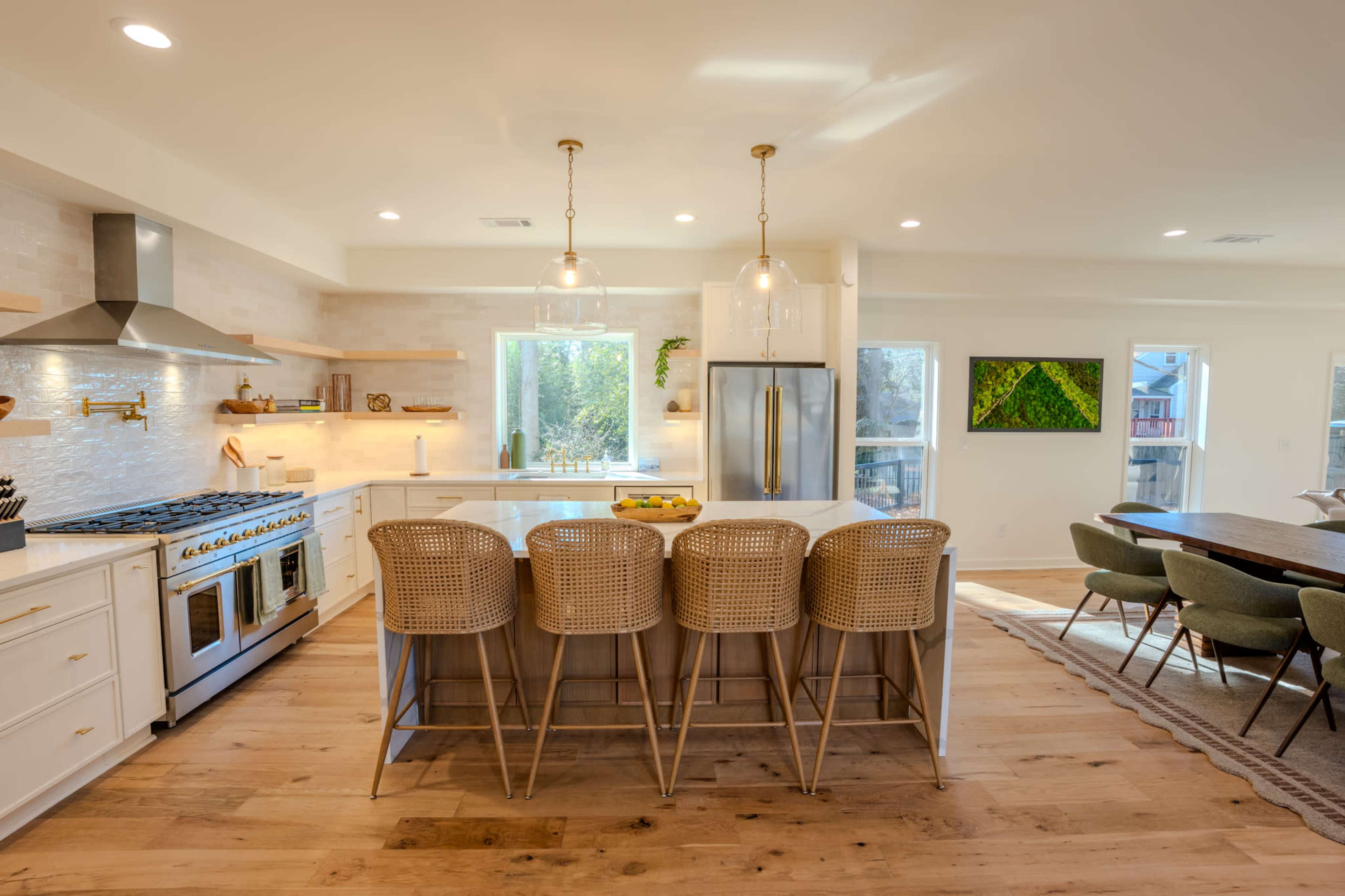 The image shows a modern kitchen with white cabinetry, a large island with four rattan bar stools, and stainless steel appliances.