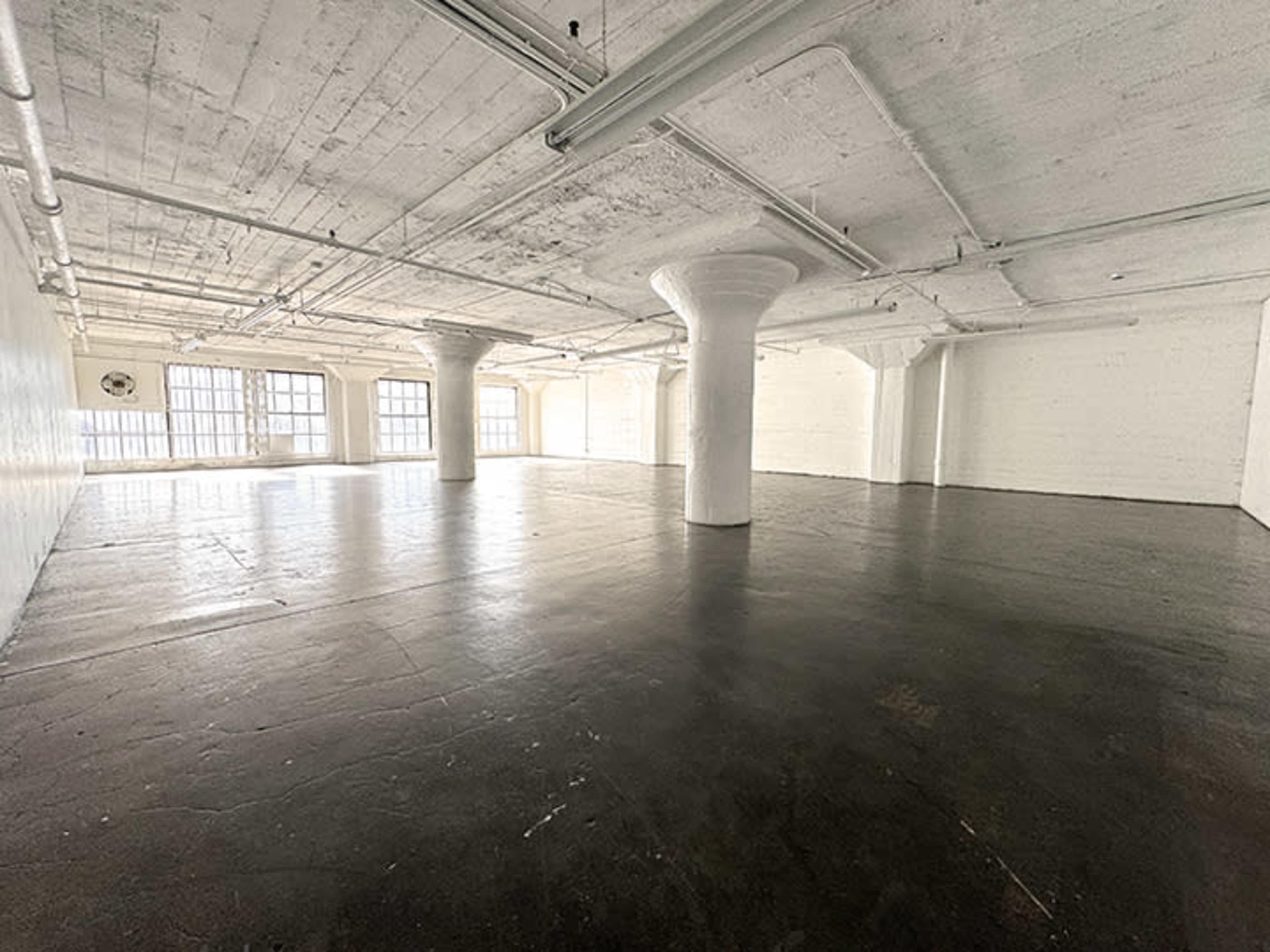 A large, empty industrial space with concrete flooring and tall windows.