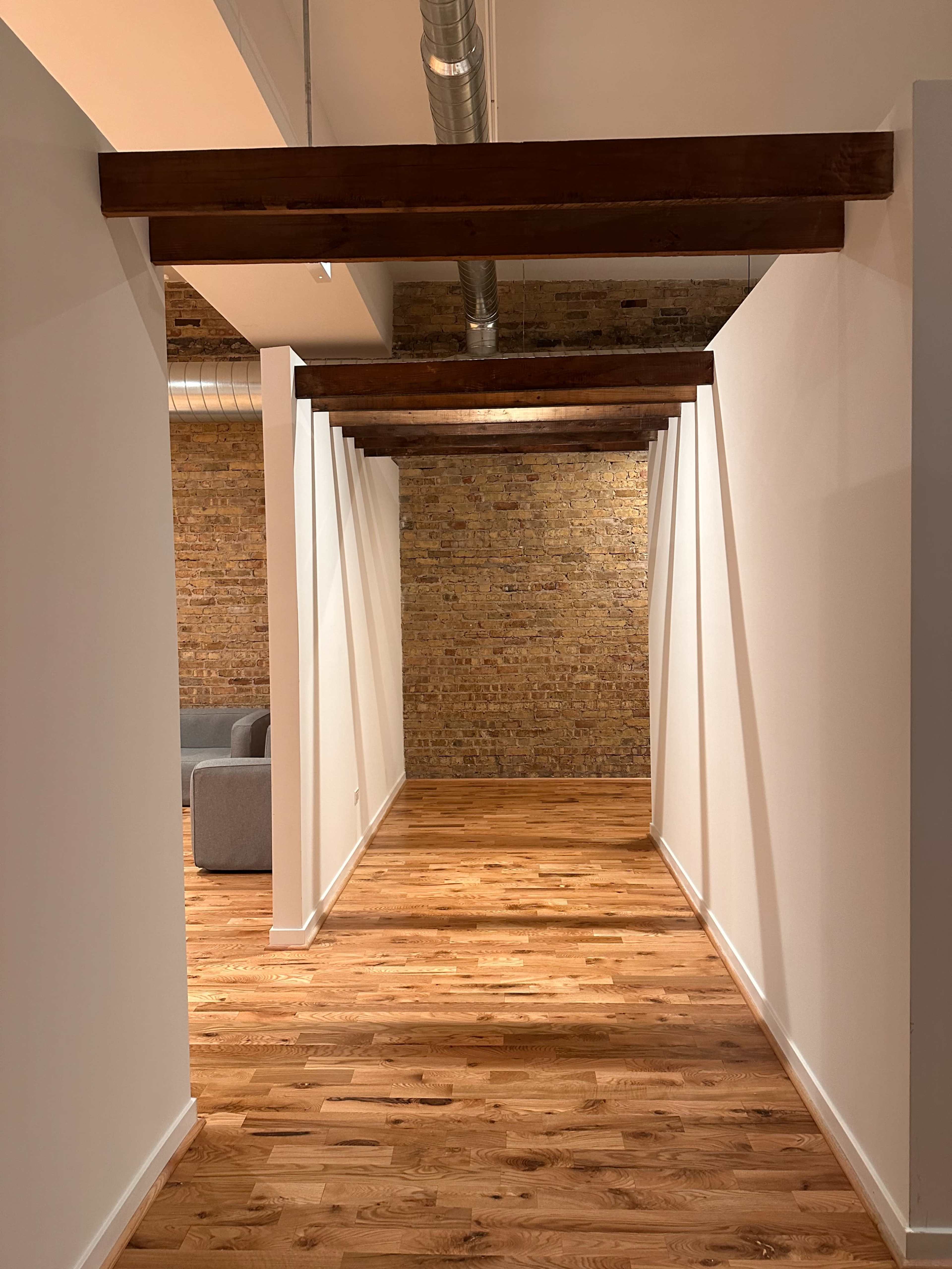 A hallway features wooden beams and white walls, leading to a brick wall at the far end.
