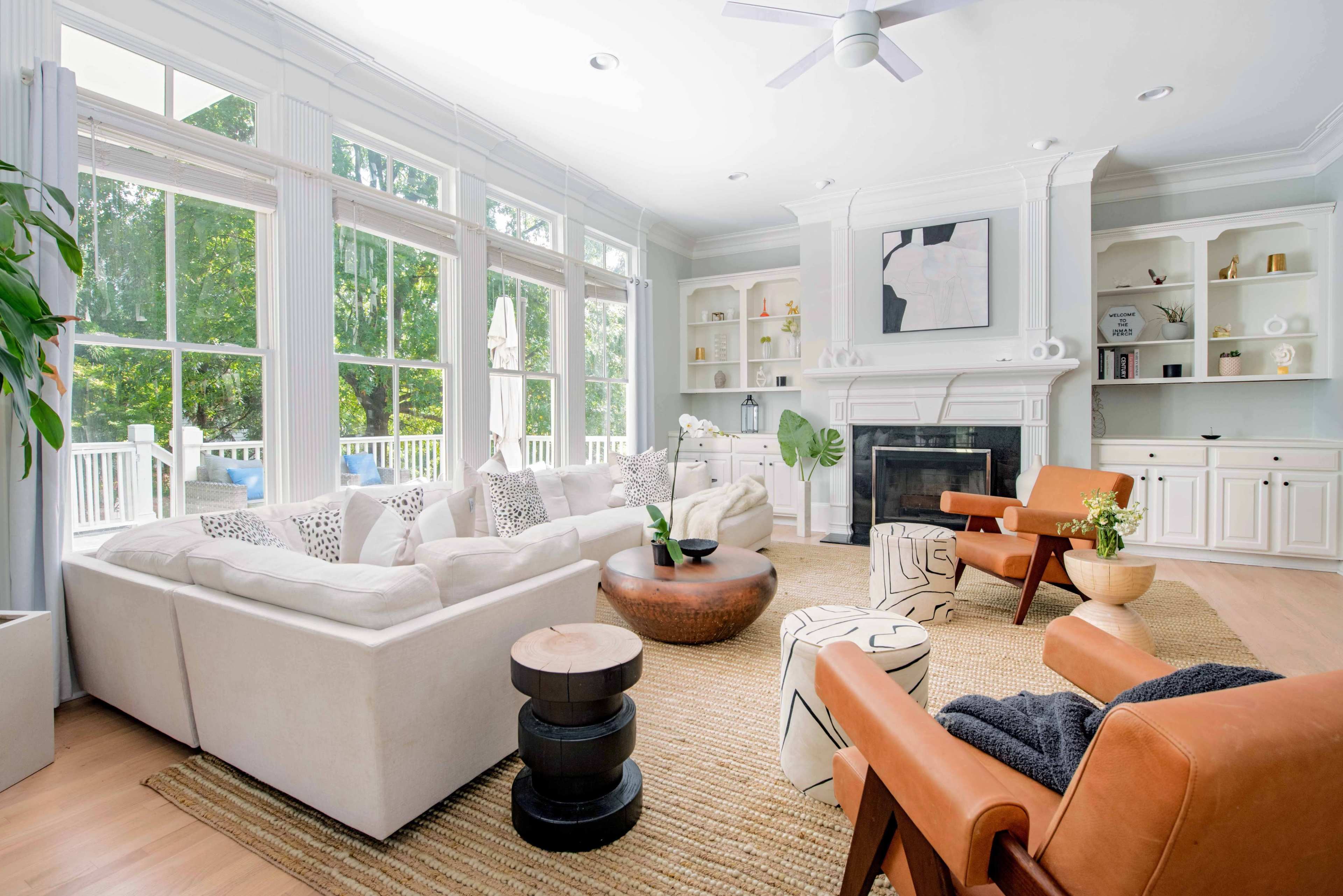 The living room features a large white sectional sofa, a round coffee table, and two armchairs, with large windows that provide ample natural light and a view of the outdoors.
