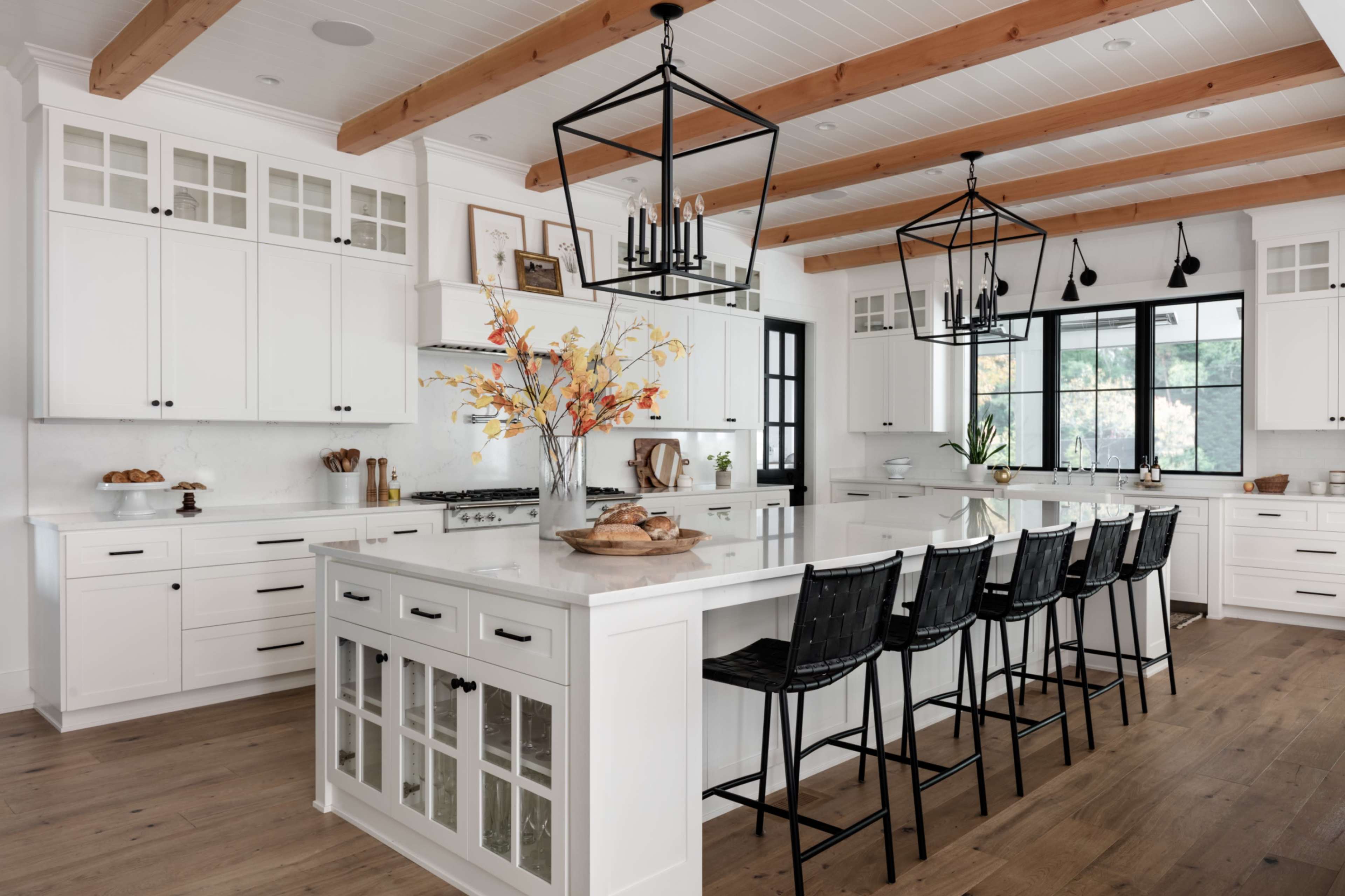 The image shows a modern kitchen with white cabinetry, an island featuring seating, and wooden beams across the ceiling.