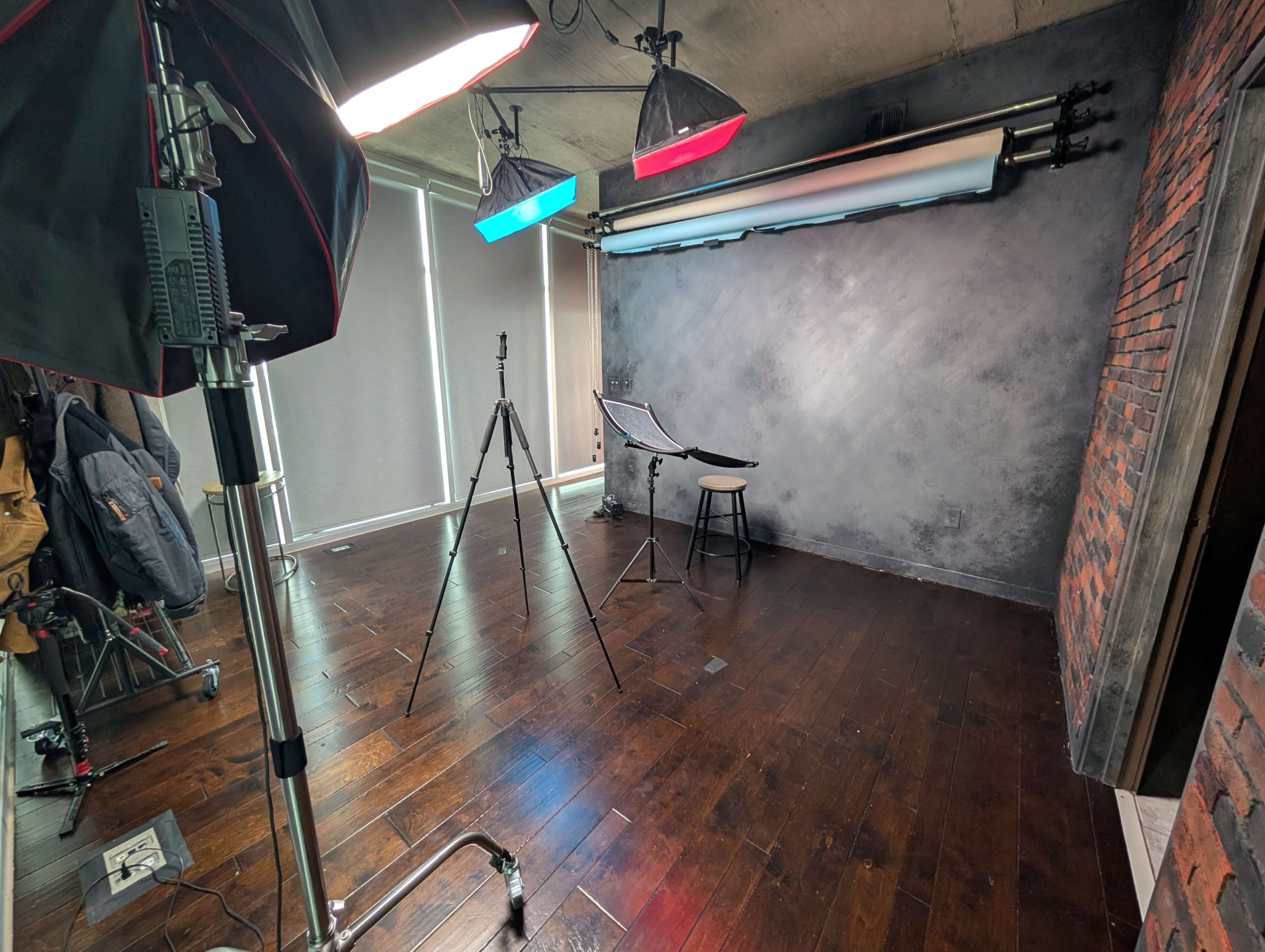 The image shows a photography studio with a stool, backdrop, lighting equipment, and a hardwood floor.