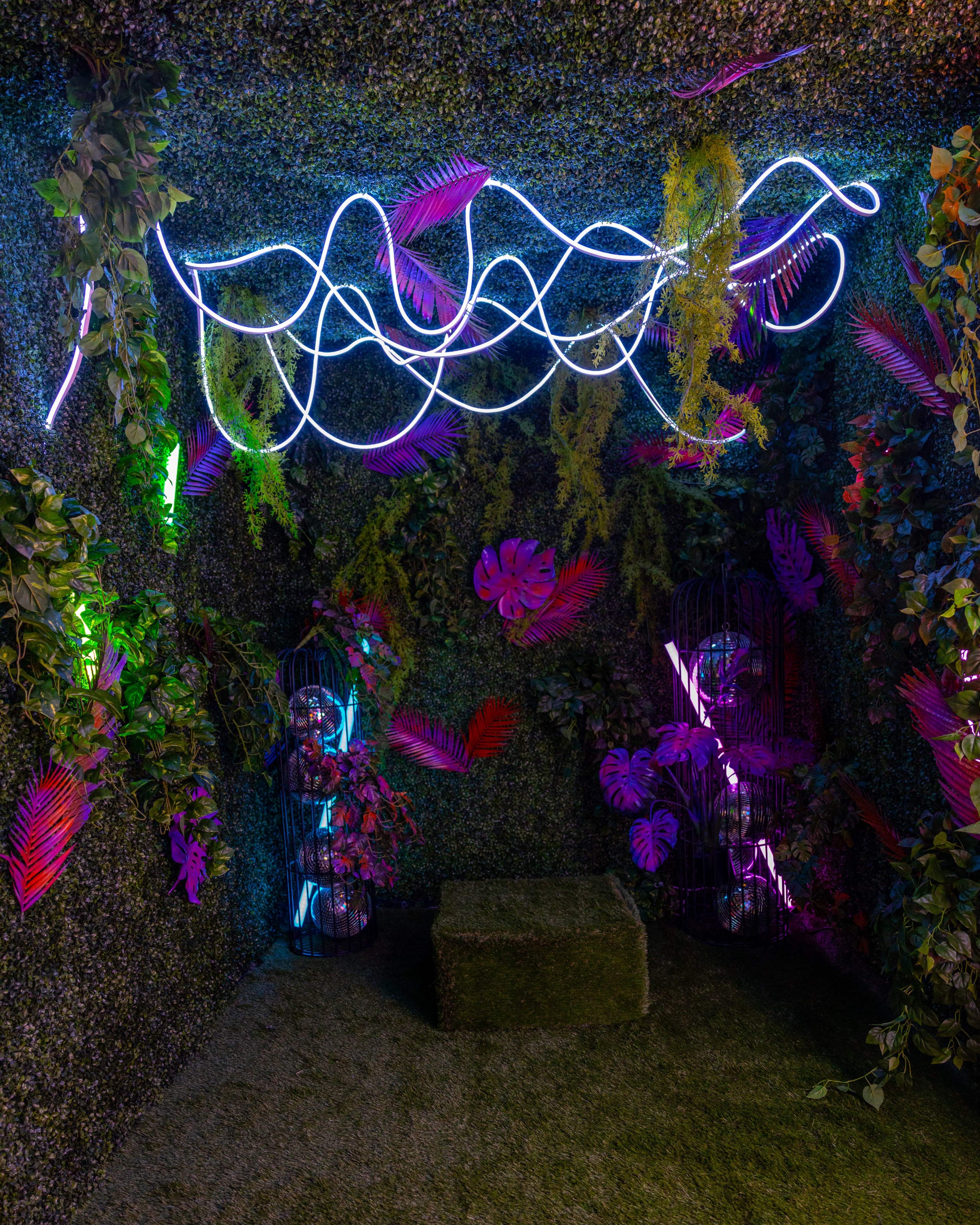 An enclosed space with vibrant artificial foliage, neon light decorations, and illuminated plants.
