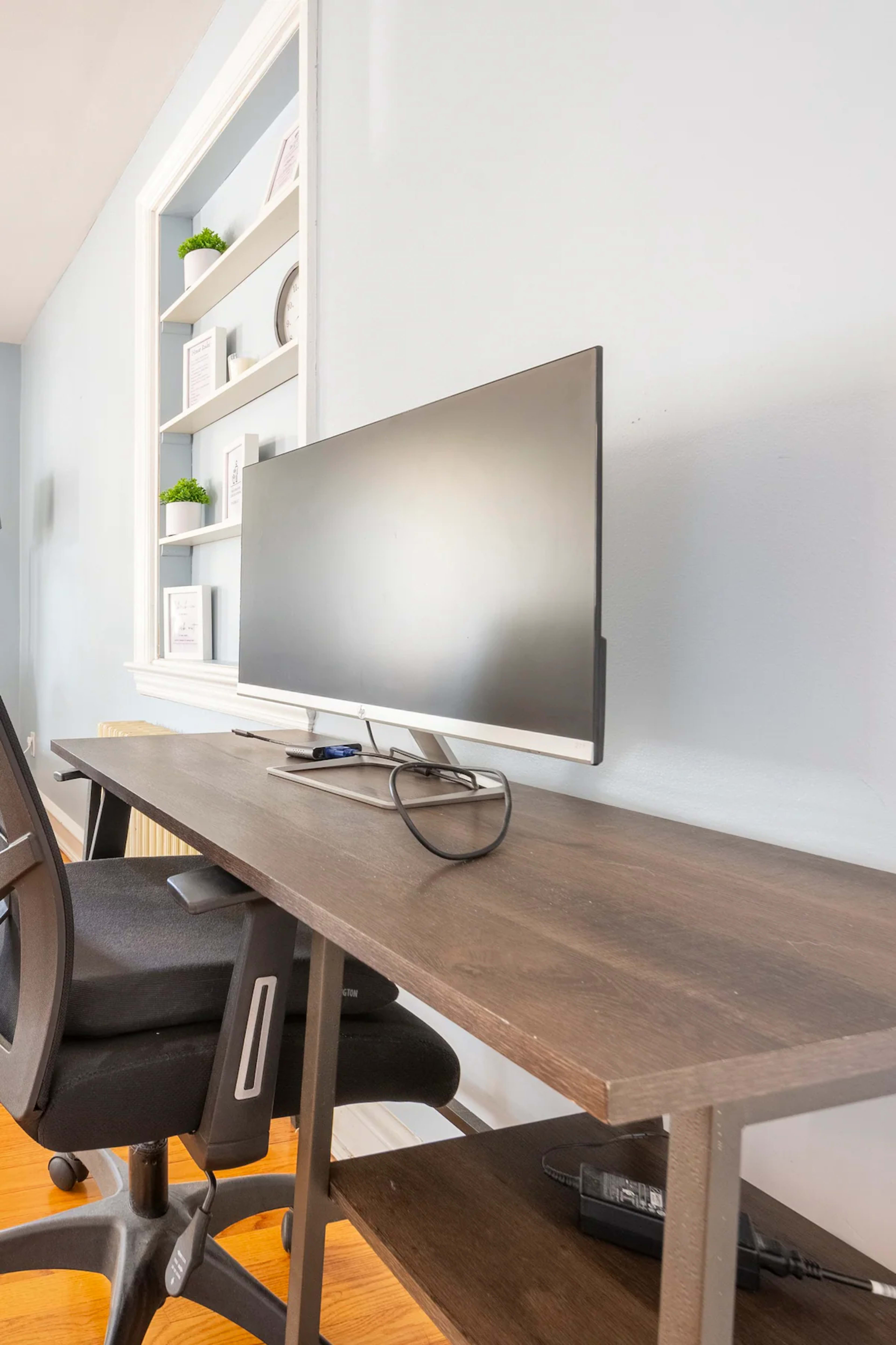 A modern office setup featuring a sleek monitor on a wooden desk against a light blue wall.