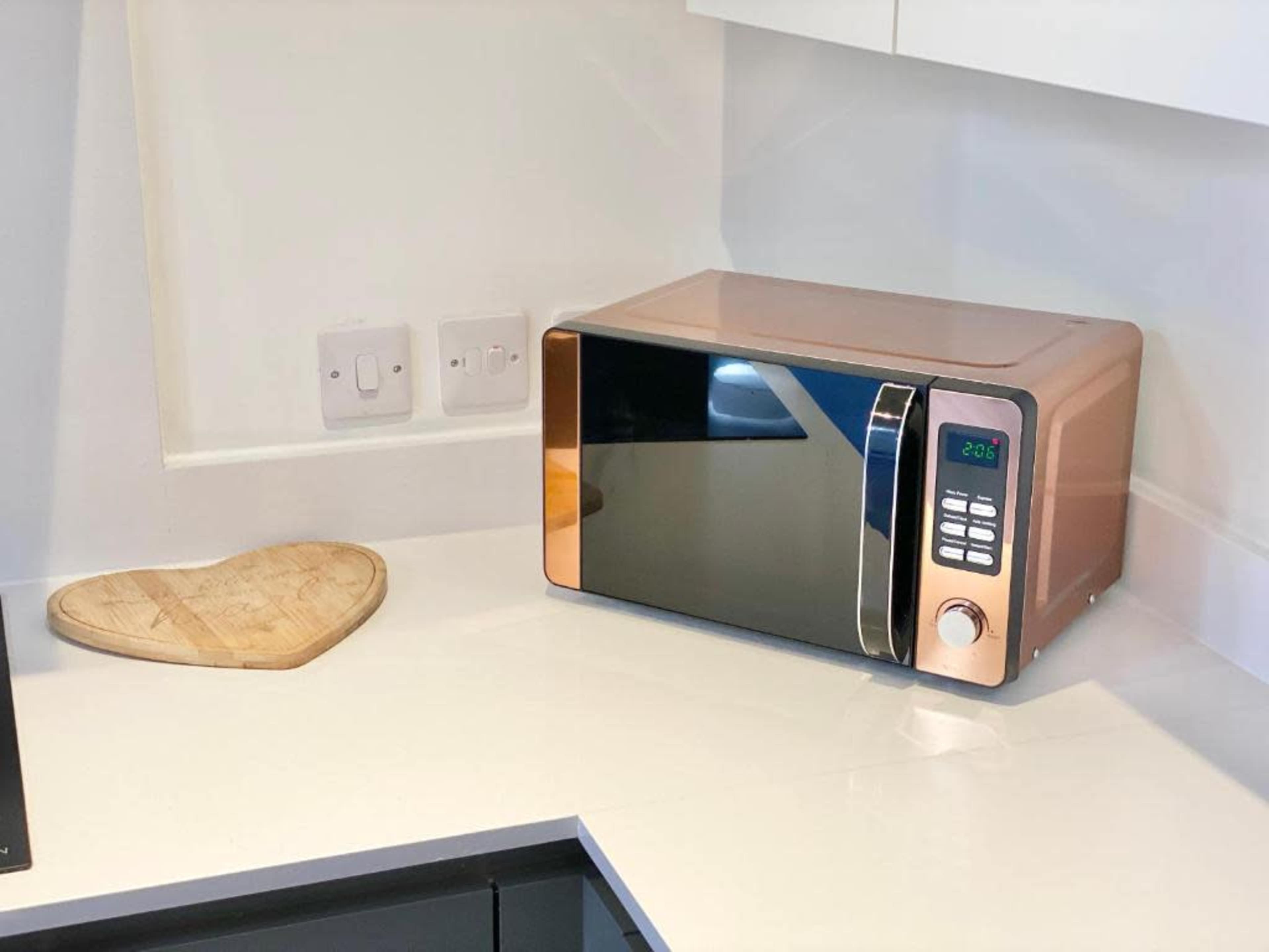 A copper-colored microwave sits on a countertop beside a heart-shaped cutting board.