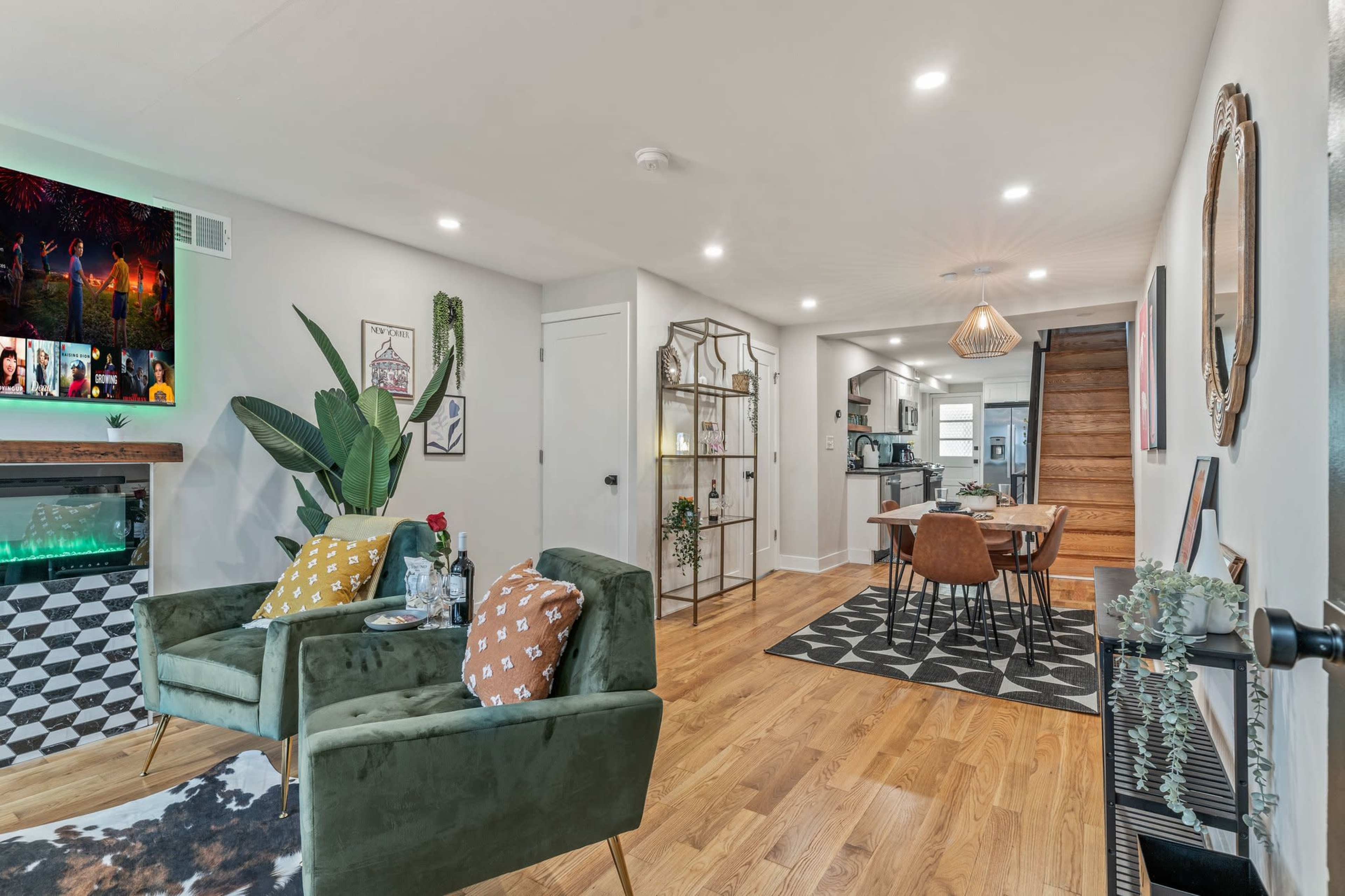 The living area features green armchairs, a small table with drinks, a decorative bookshelf, and a view into the dining area and kitchen.