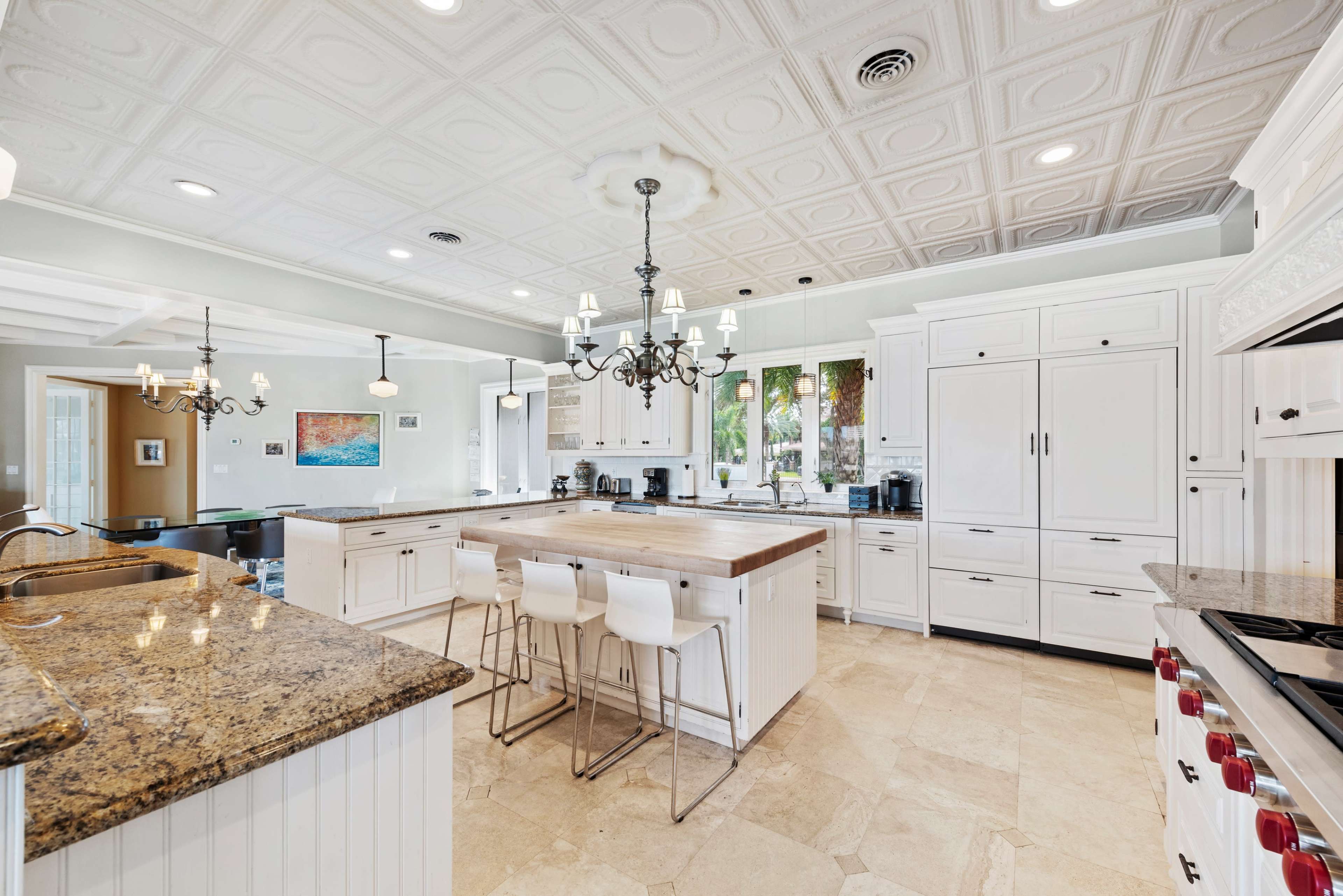 A spacious modern kitchen features white cabinetry, a large wooden island, and granite countertops, with a chandelier and multiple appliances throughout.