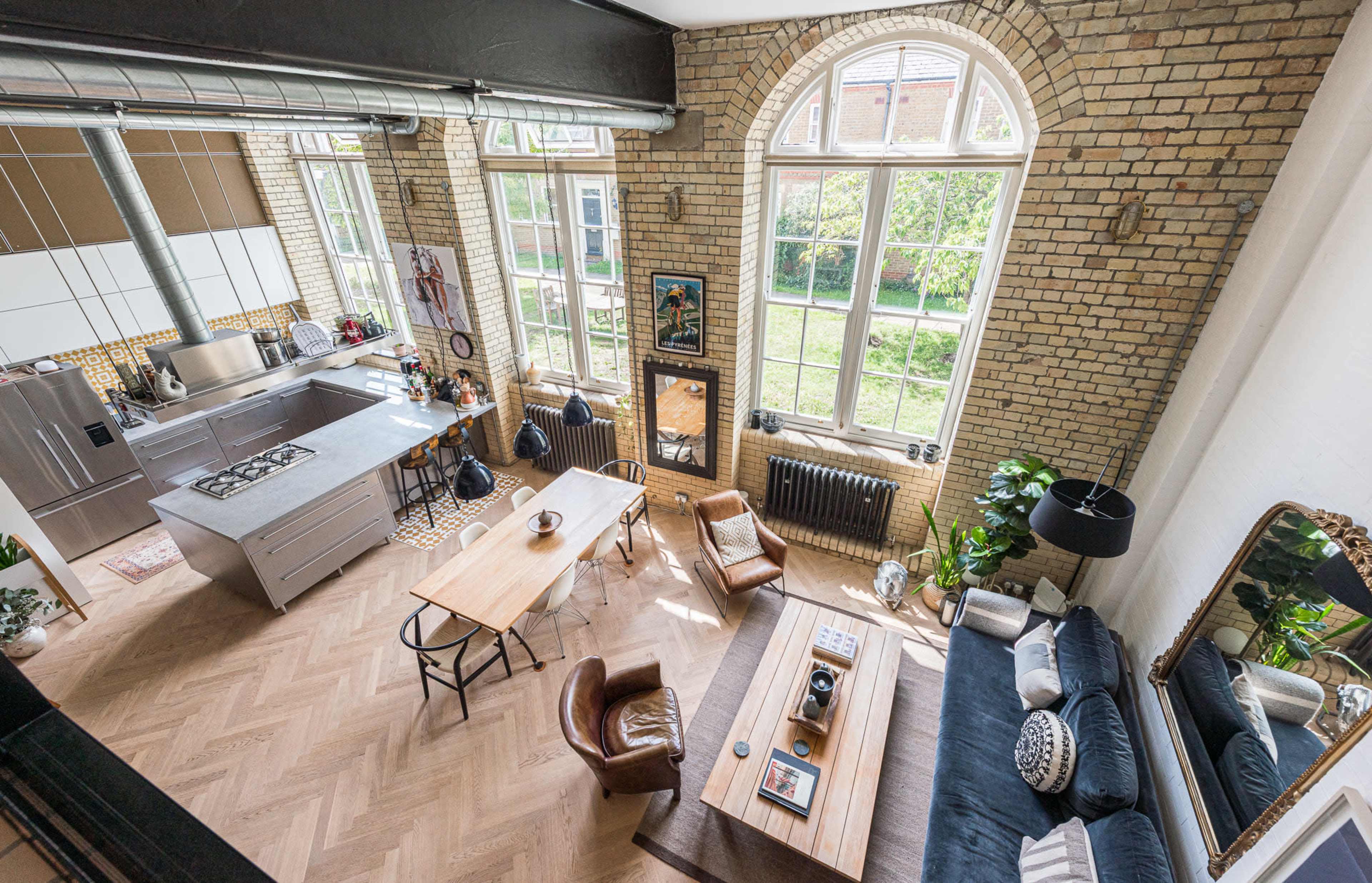 The image shows a spacious, modern living area with large windows, featuring a kitchen, dining table, and comfortable seating.