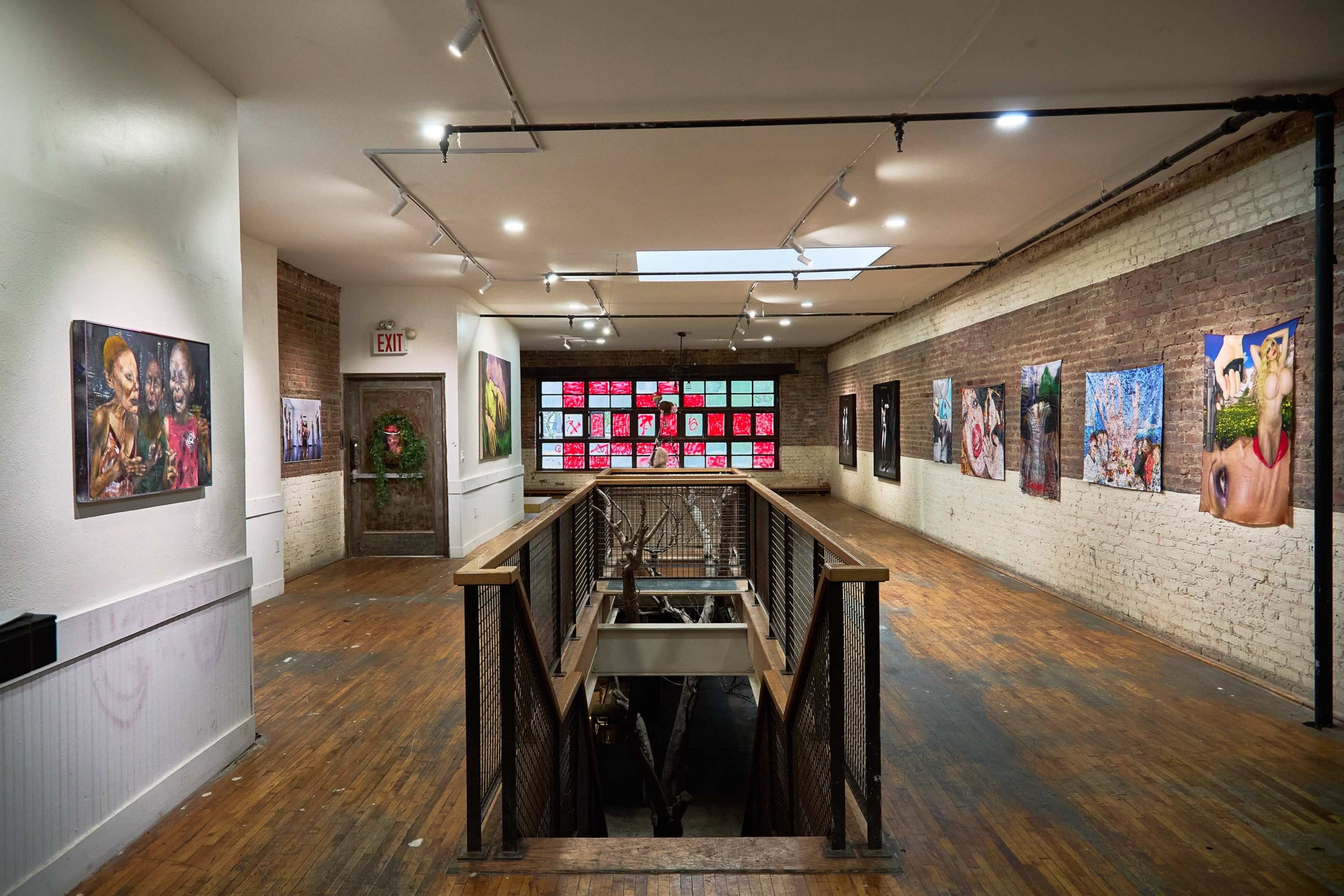 The image shows an art gallery with vibrant artwork displayed on the walls, wooden flooring, and a large window featuring colorful panels.