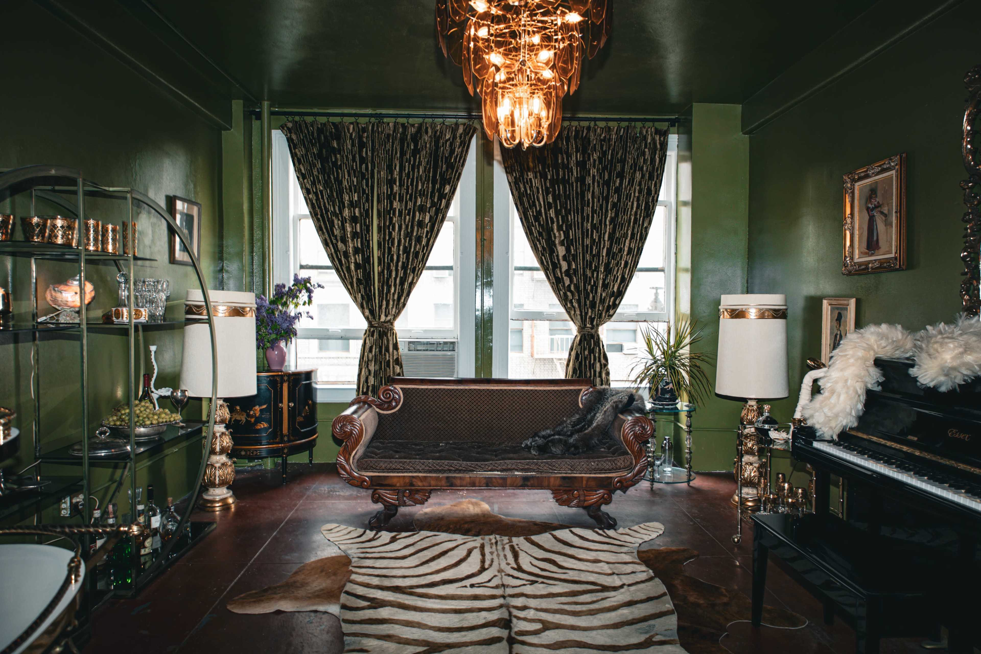 The scene features a vintage living room with dark green walls, a large chandelier, elegant curtains, a plush couch, and a piano against the wall.