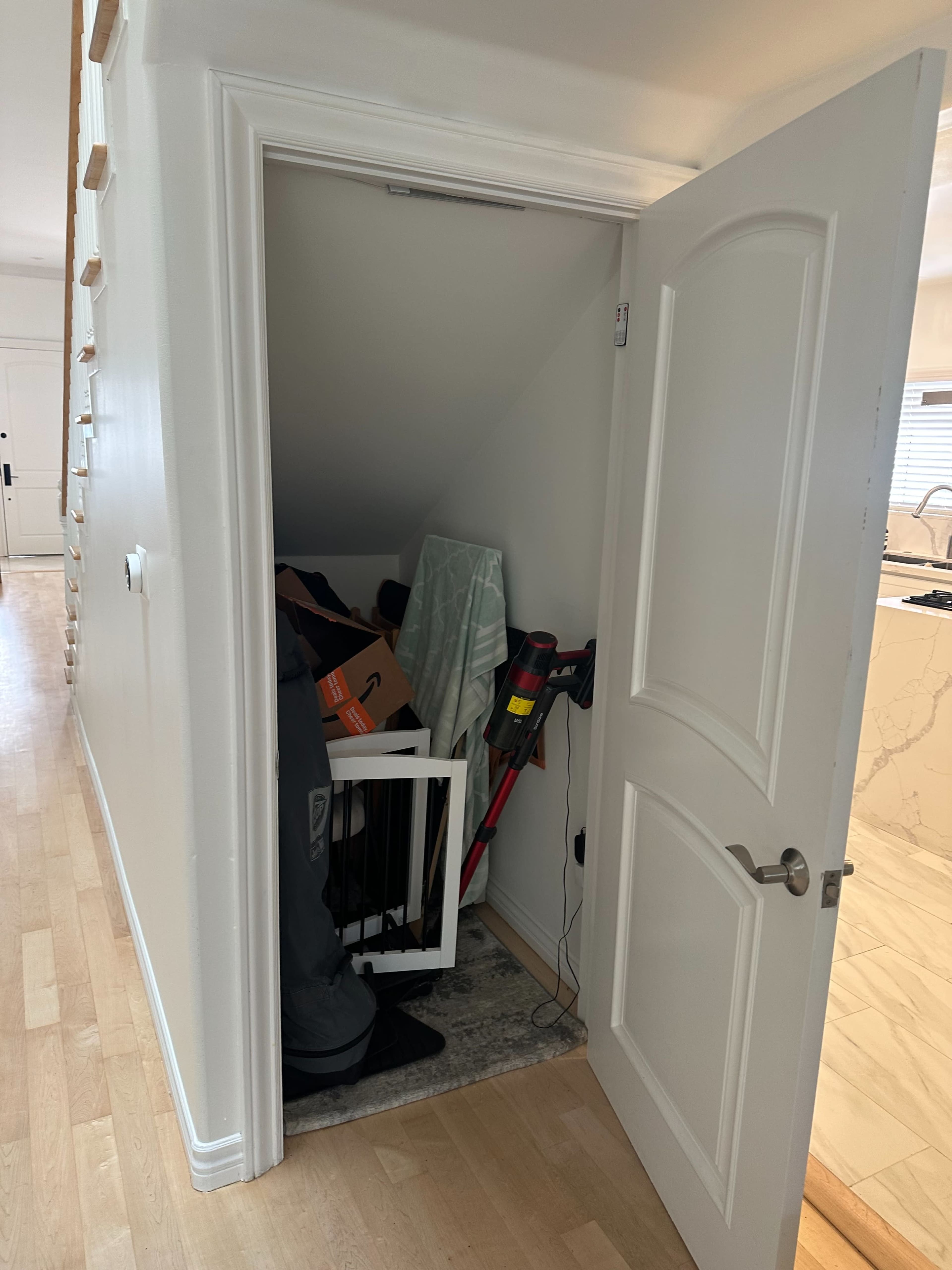 The image shows an open closet filled with various items, including boxes and cleaning equipment, located in a hallway.
