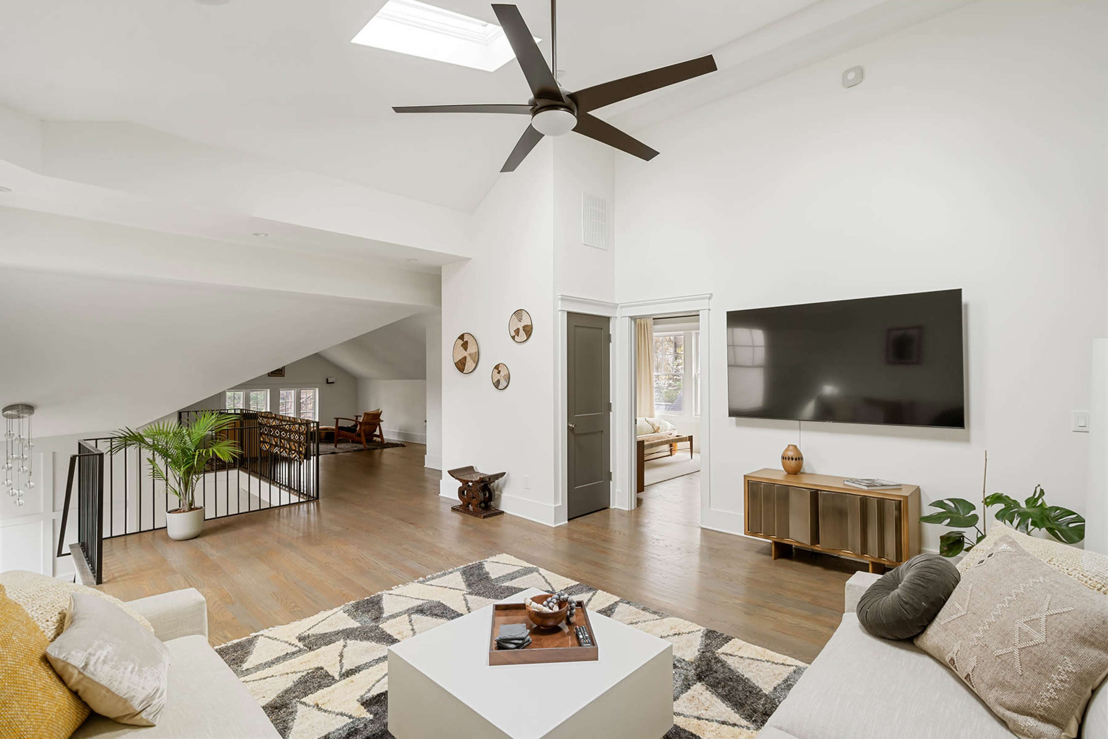 The living area features a modern design with a ceiling fan, a large TV mounted on the wall, and a cozy seating arrangement.