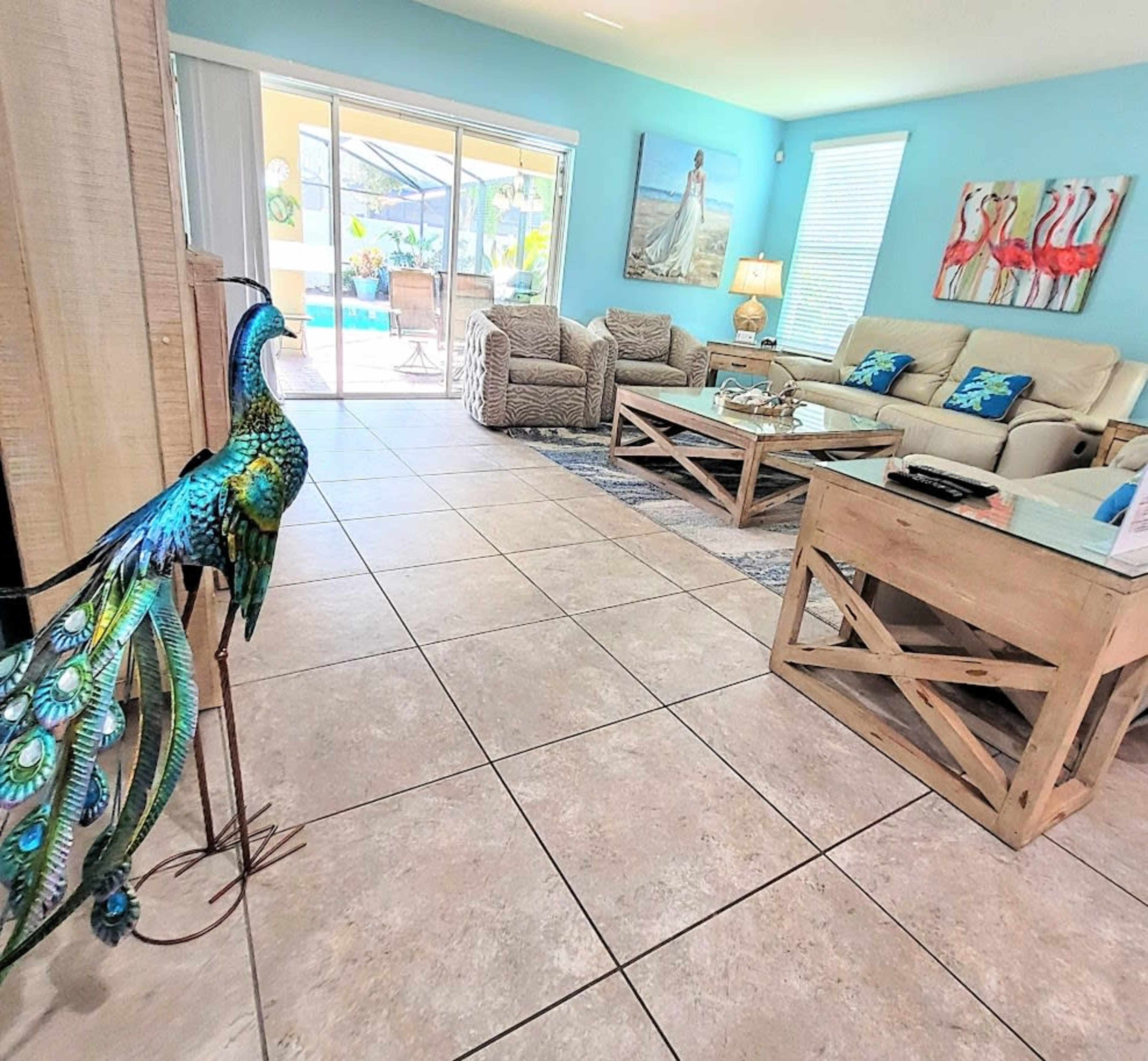 A living room with beige furniture, a decorative peacock sculpture, and sliding glass doors leading to a pool area.