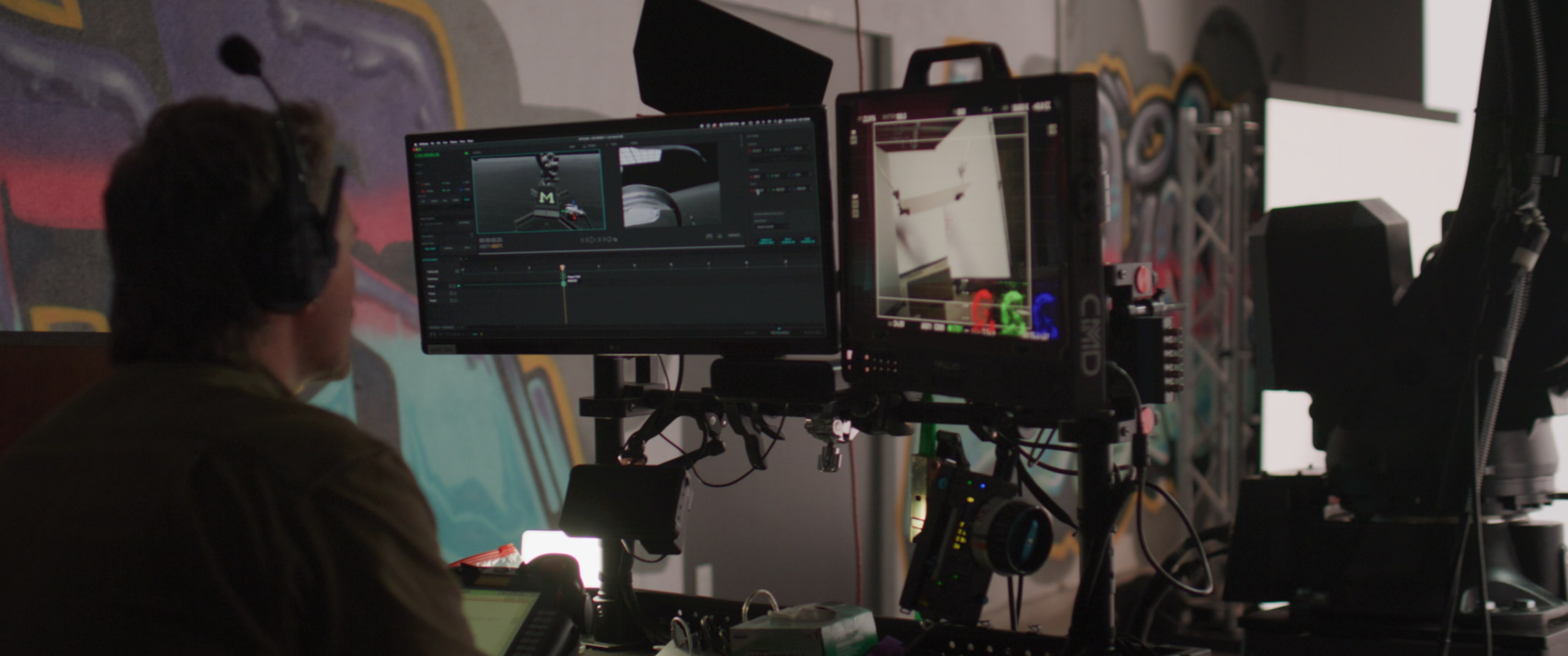 A person works at a dual-monitor setup showing video editing software, with a colorful graffiti background.