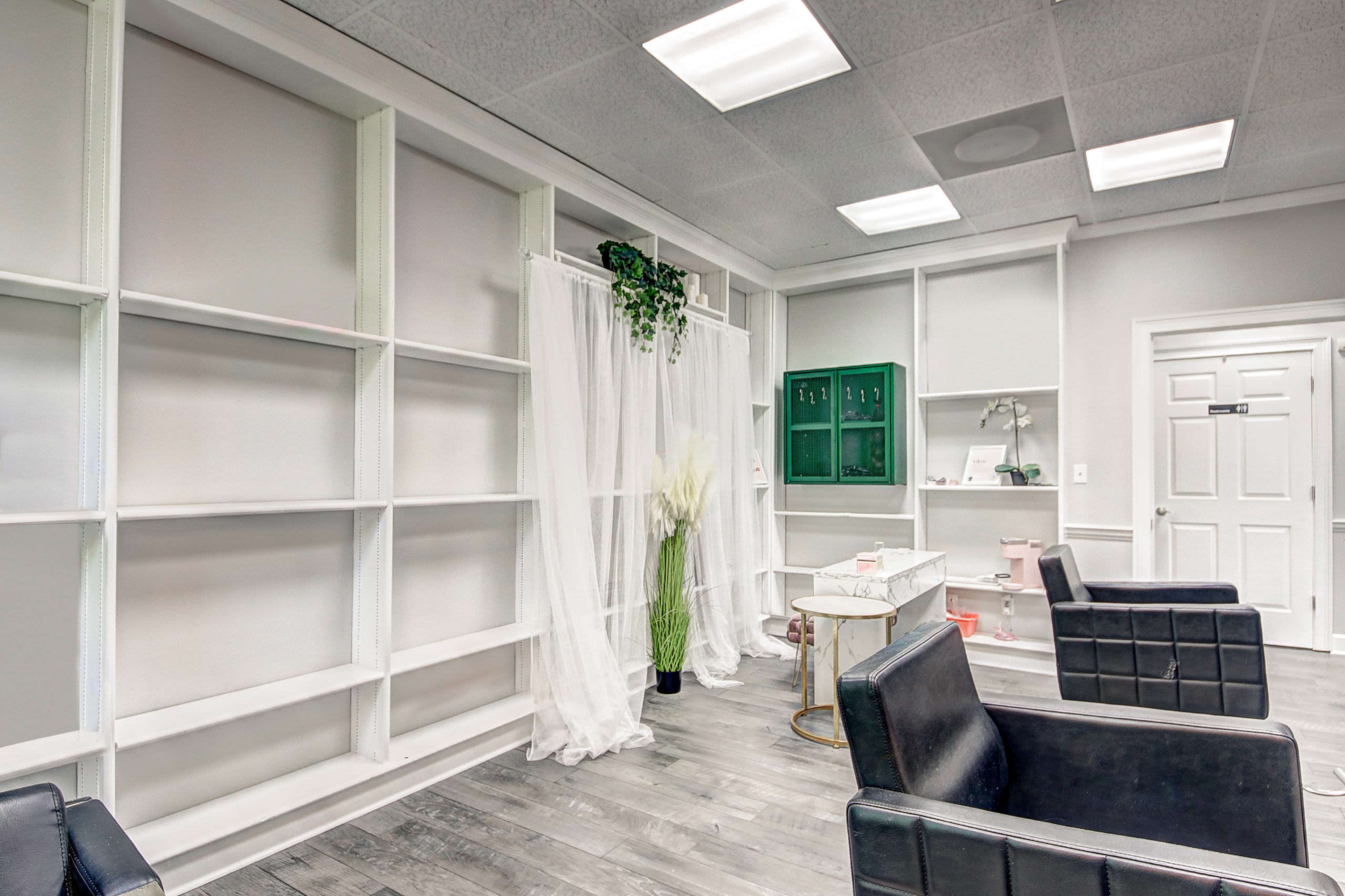 A spacious interior features white shelves, a sheer curtain, and black leather chairs against a light-colored floor.
