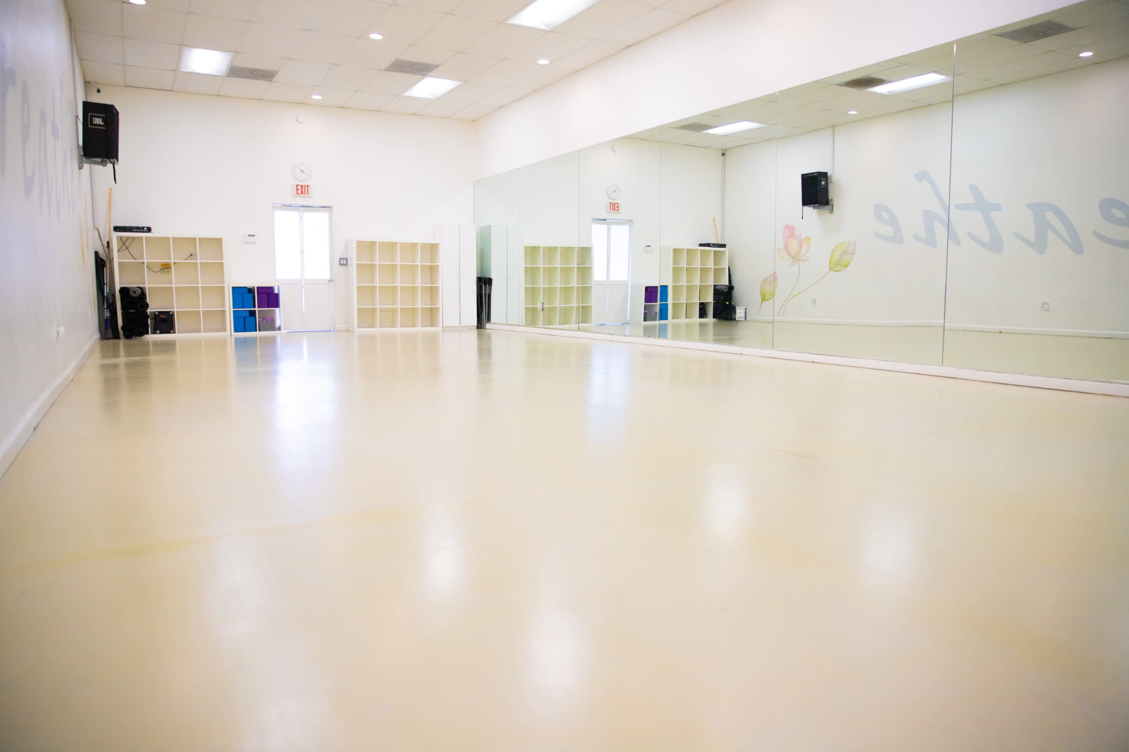 The image shows a spacious, empty dance studio with a mirrored wall and light-colored flooring.