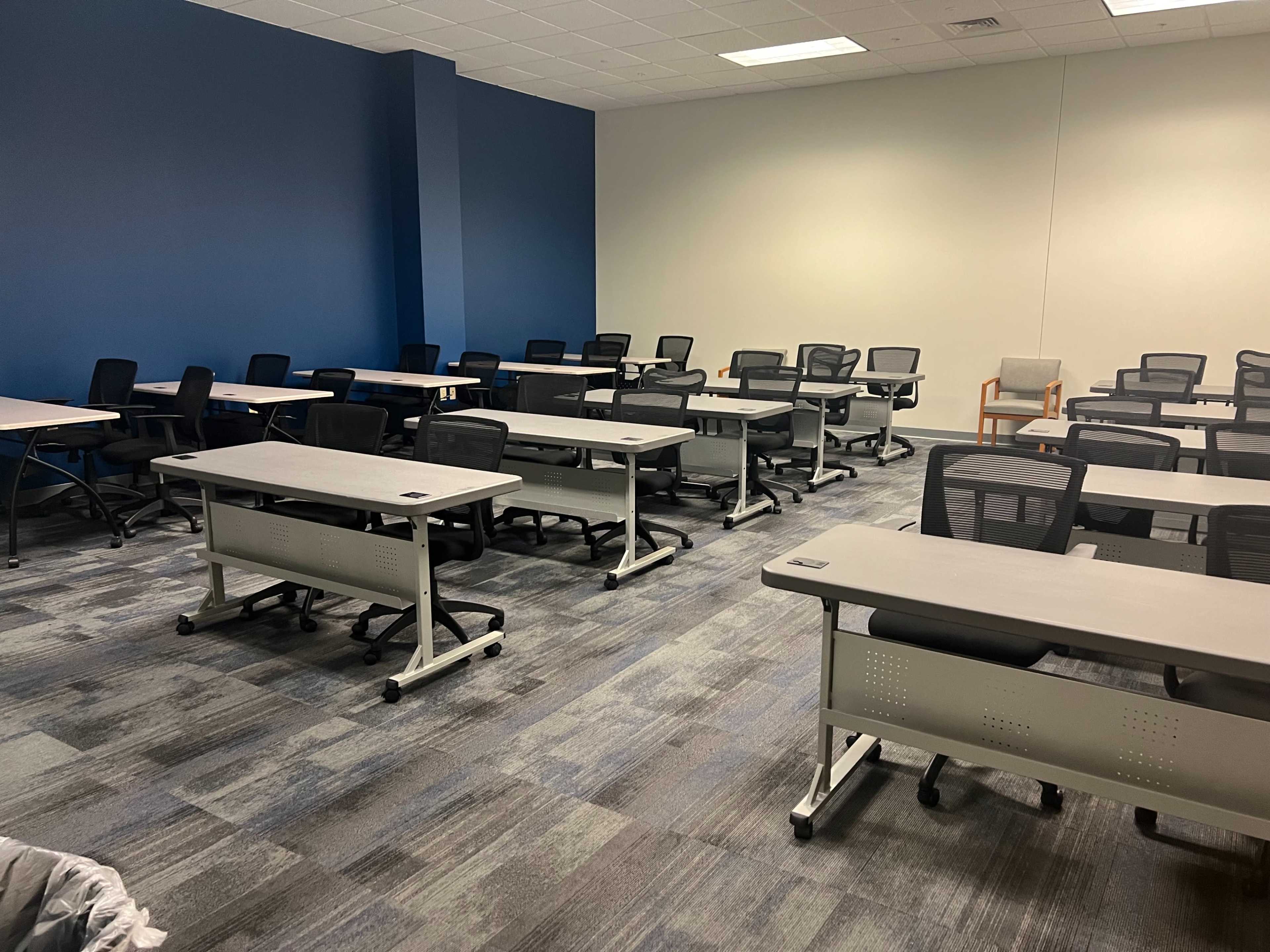 A classroom is set up with multiple rows of desks and chairs arranged for instruction.