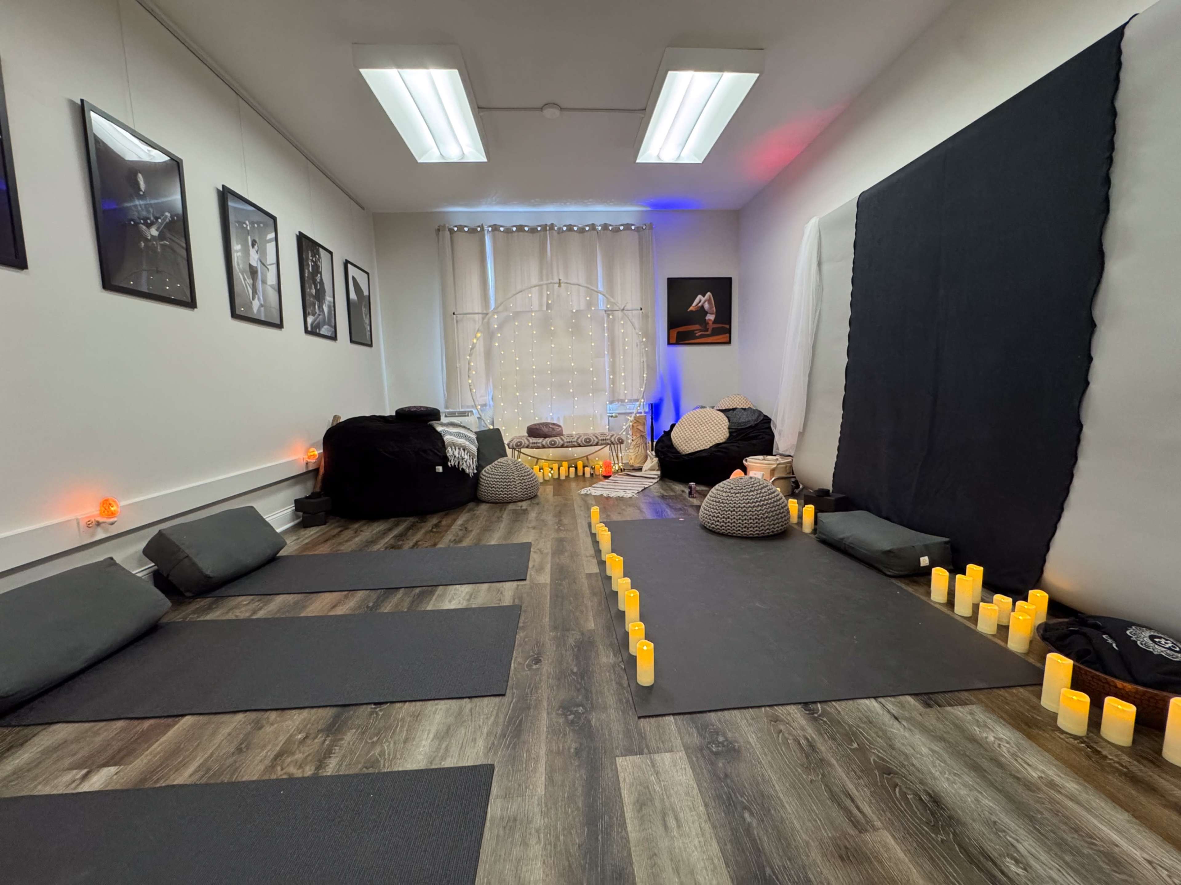 The image shows a yoga and meditation studio with mats on the floor, bean bags, and candles arranged along the edges, creating a serene atmosphere.