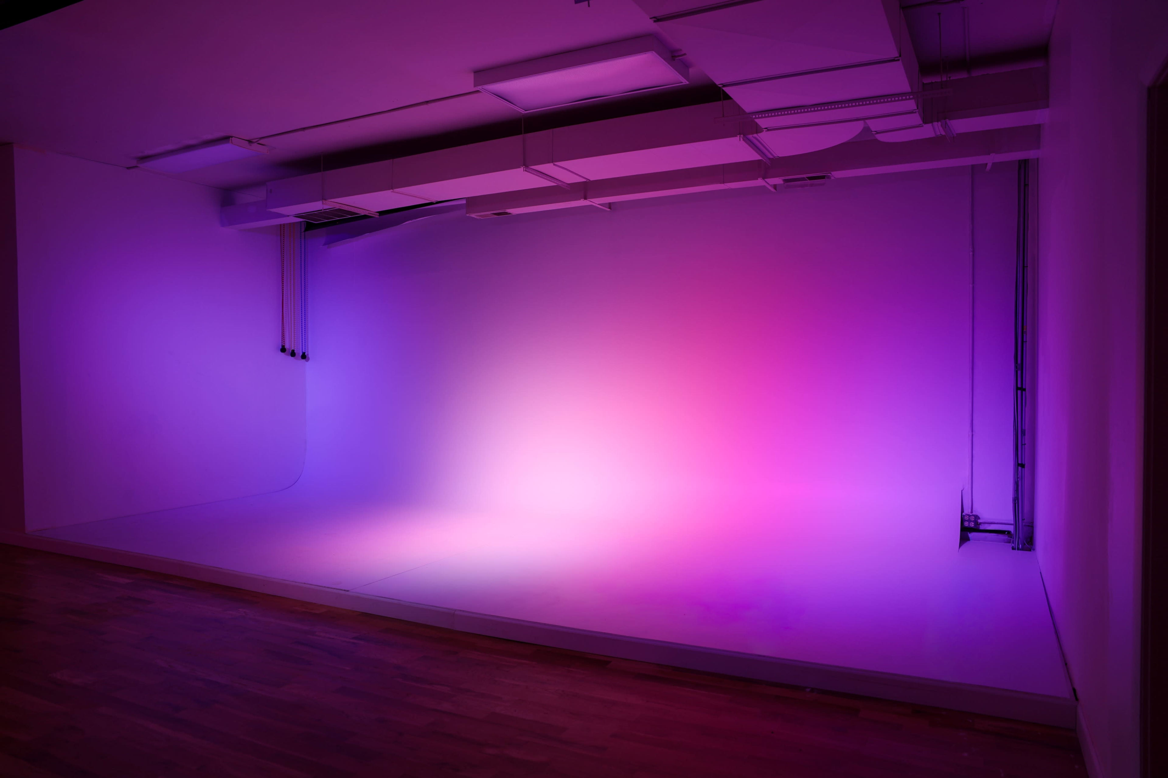 The image depicts a minimalist studio space with a gradient of purple and pink lighting on the backdrop.