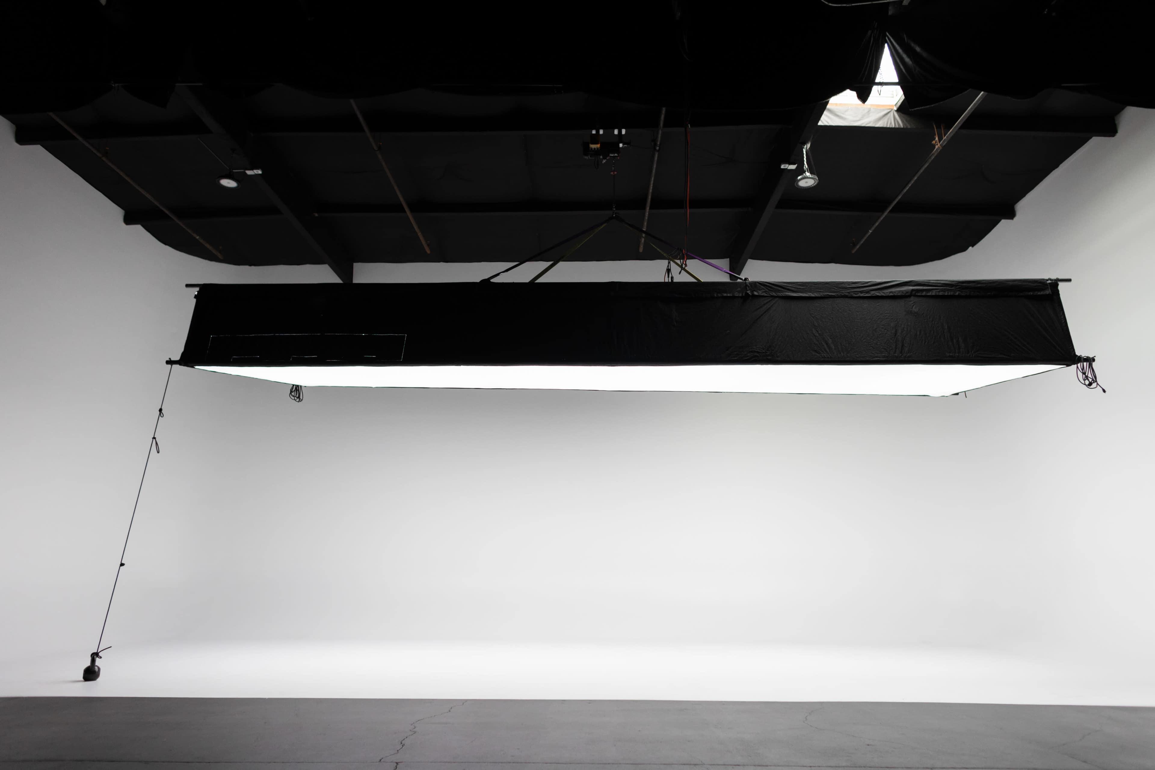 A large softbox is suspended from the ceiling in a studio with a plain white backdrop.