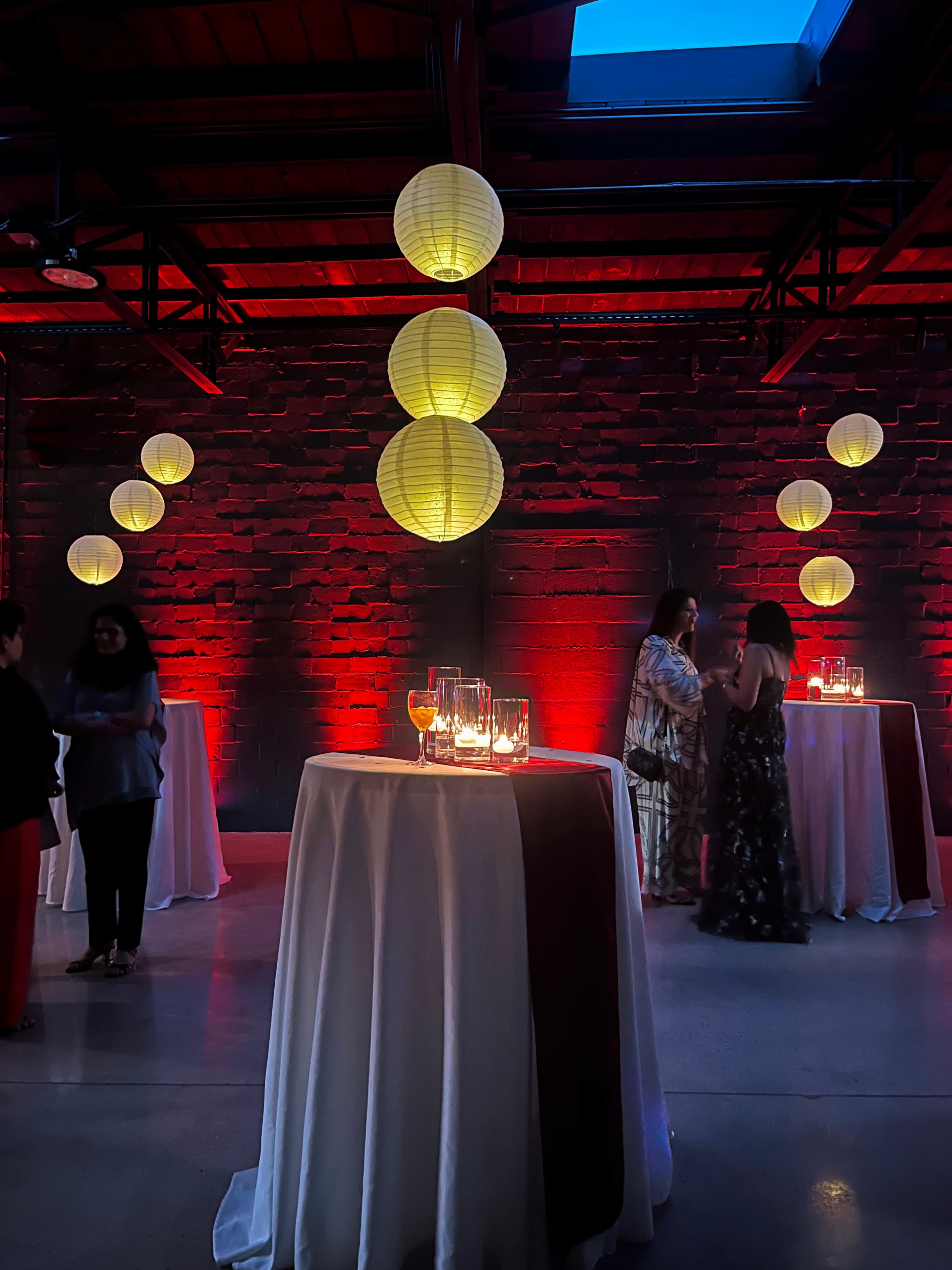 The scene features a dimly lit event space with several tables adorned with candles, and decorative paper lanterns hanging from the ceiling.