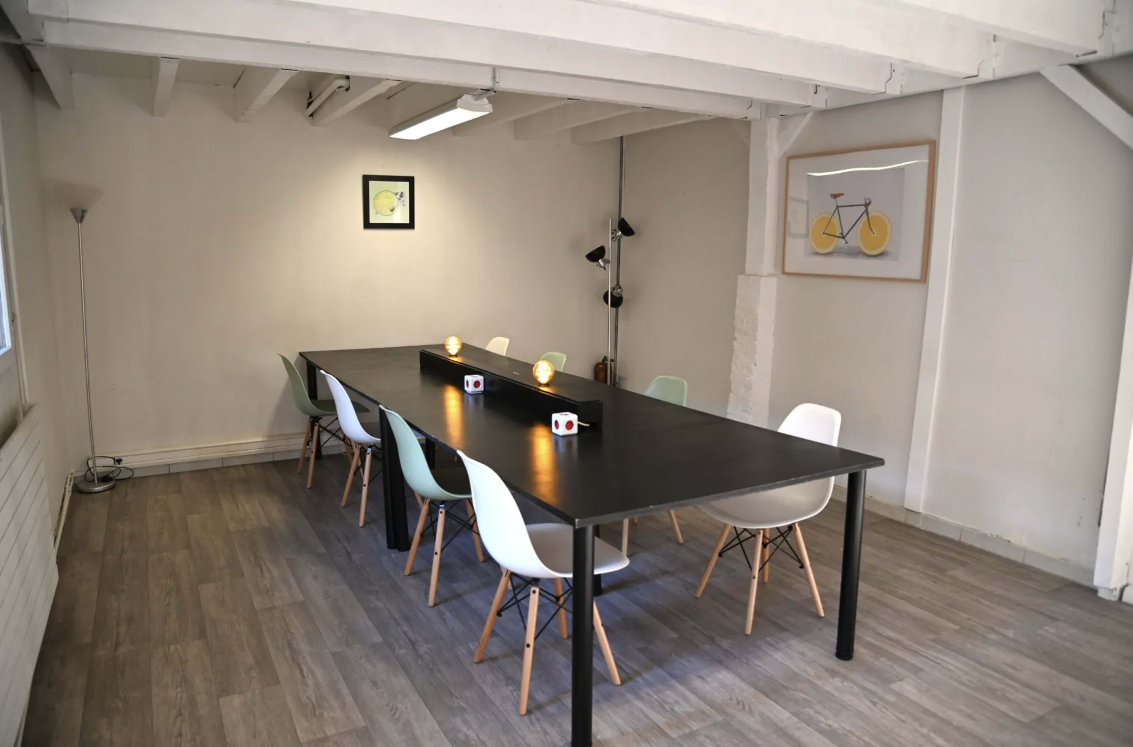 A long black table with chairs of various colors is set up in a well-lit, minimalistic room.