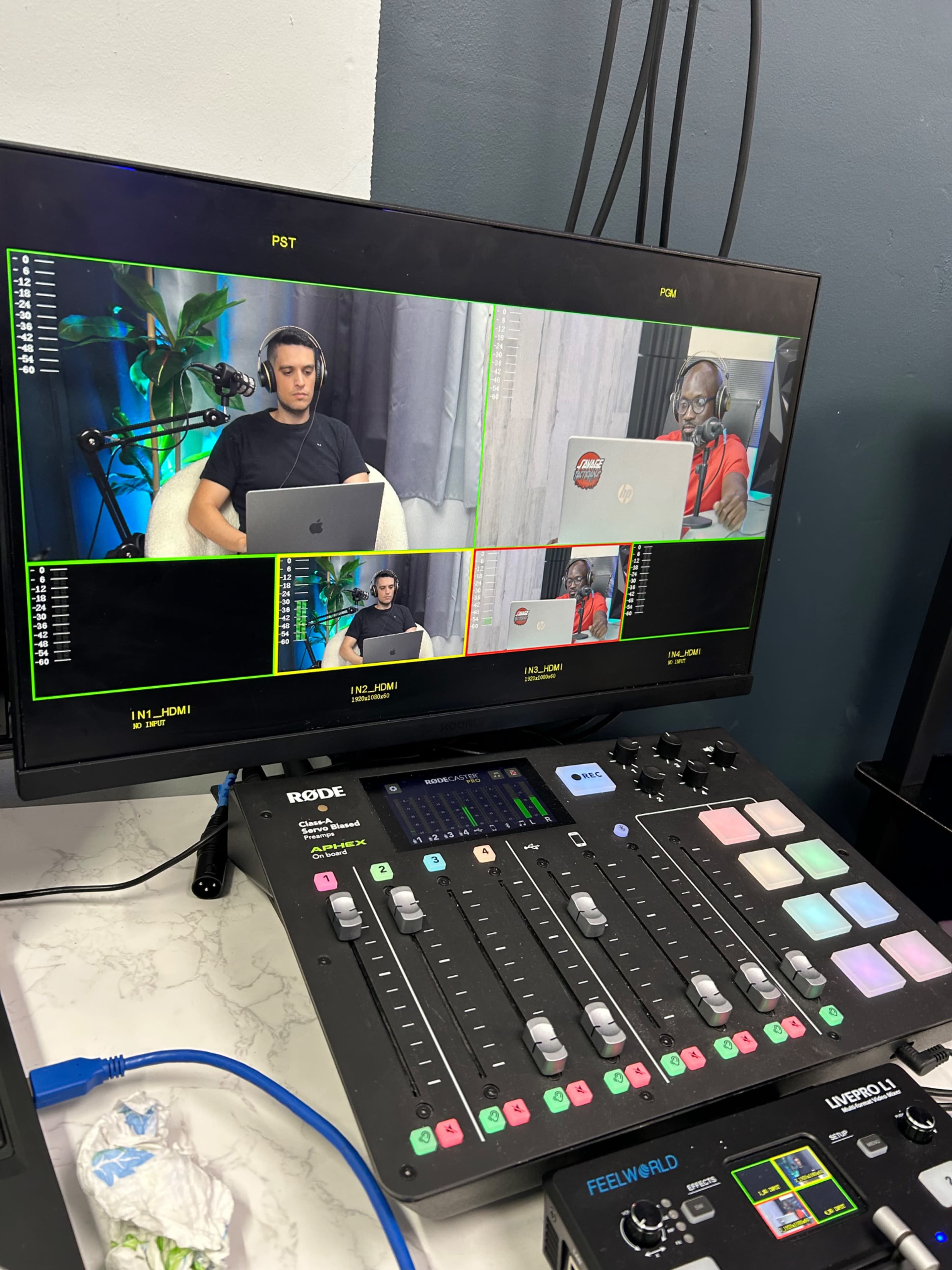 A video production setup with a monitor displaying four participants in a grid layout, along with a control panel in the foreground.