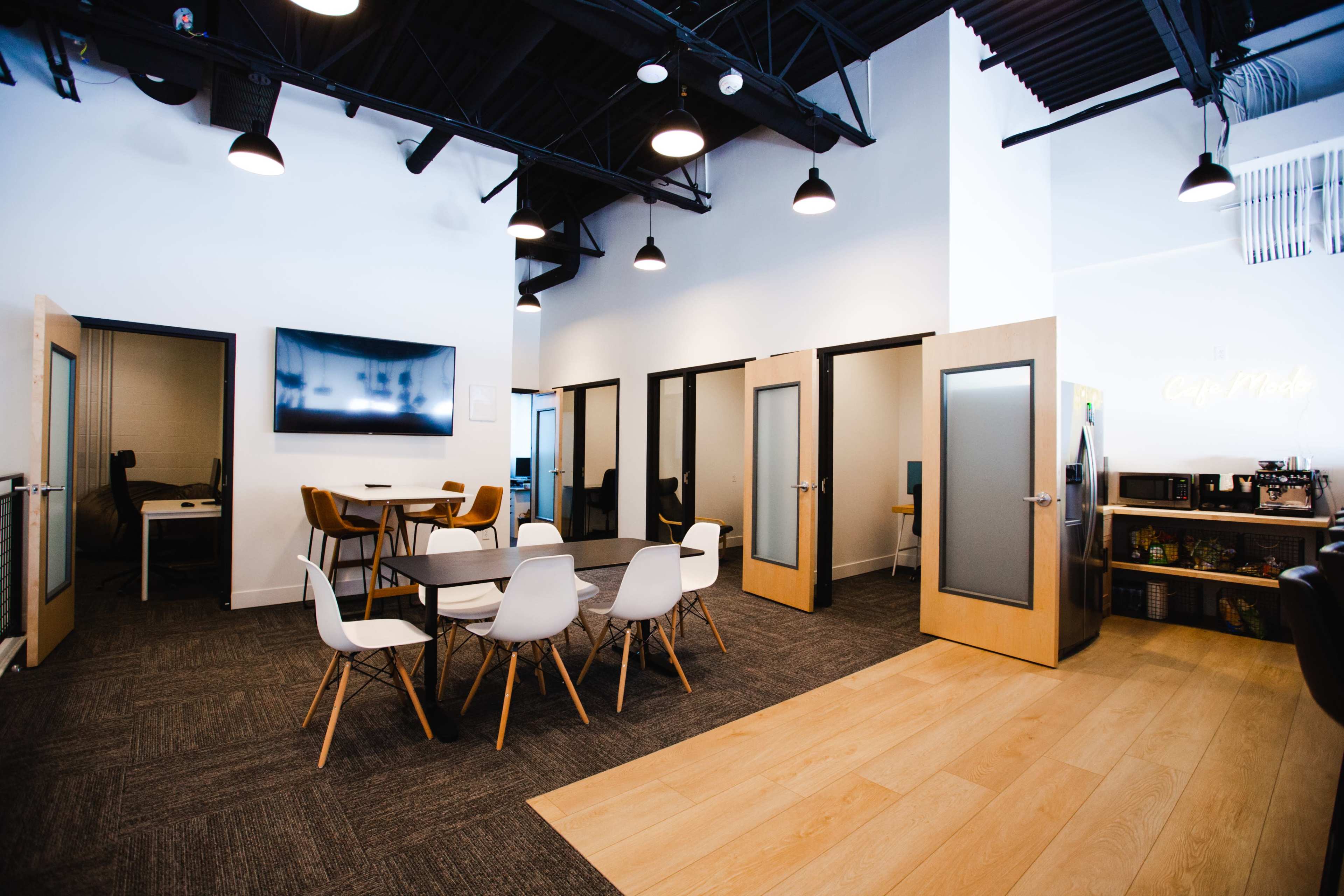 A modern office space with a table and chairs in the center, surrounded by private meeting rooms with glass doors.