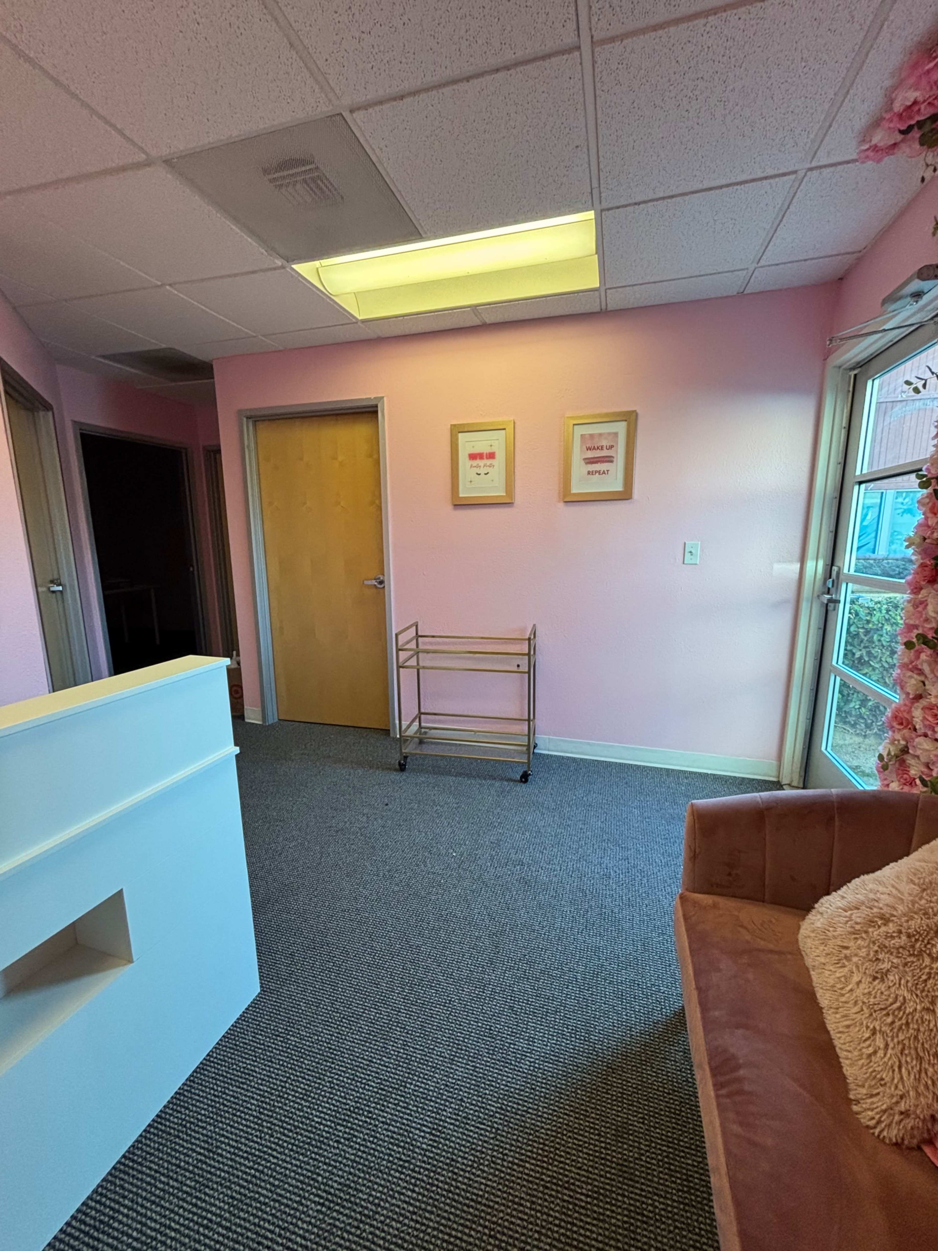 The image shows a brightly colored pink room with a reception area, a small cart against one wall, and two doorways leading to separate rooms.