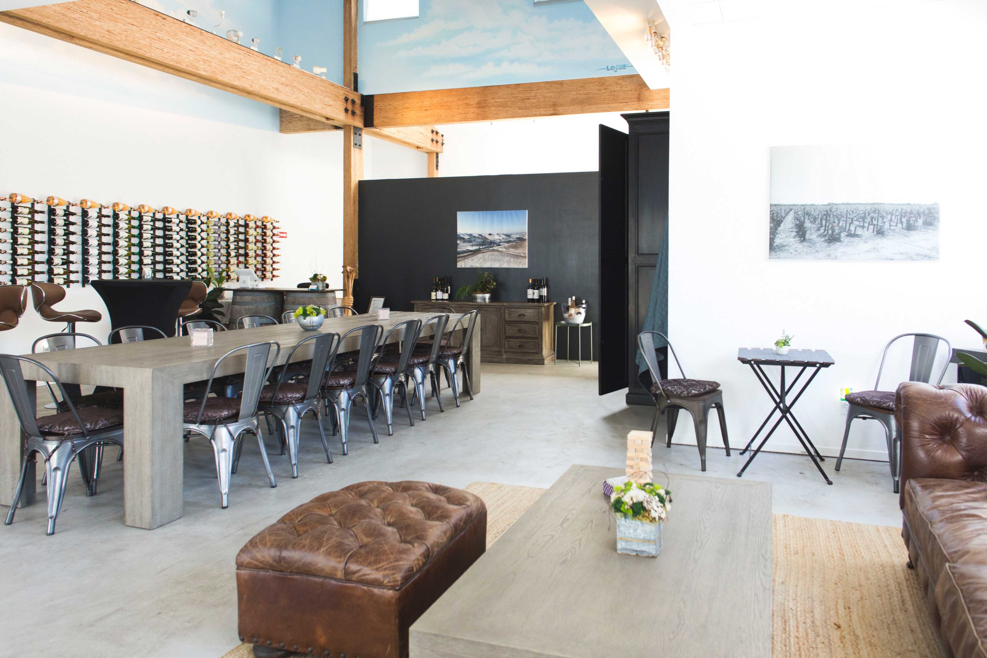 An indoor space featuring a long dining table, several chairs, and a bar area with bottles displayed on the wall.
