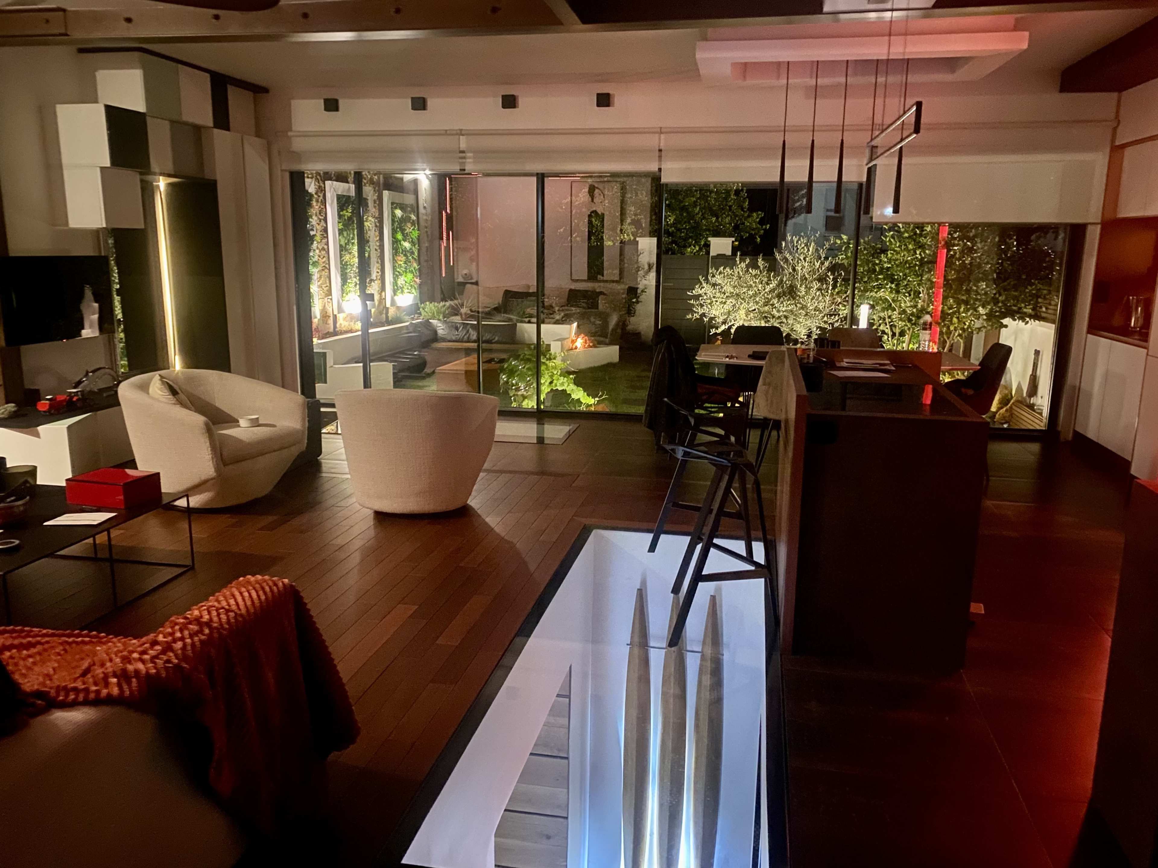 A modern living space features an open floor plan with a view of an illuminated outdoor garden and stylish furniture.