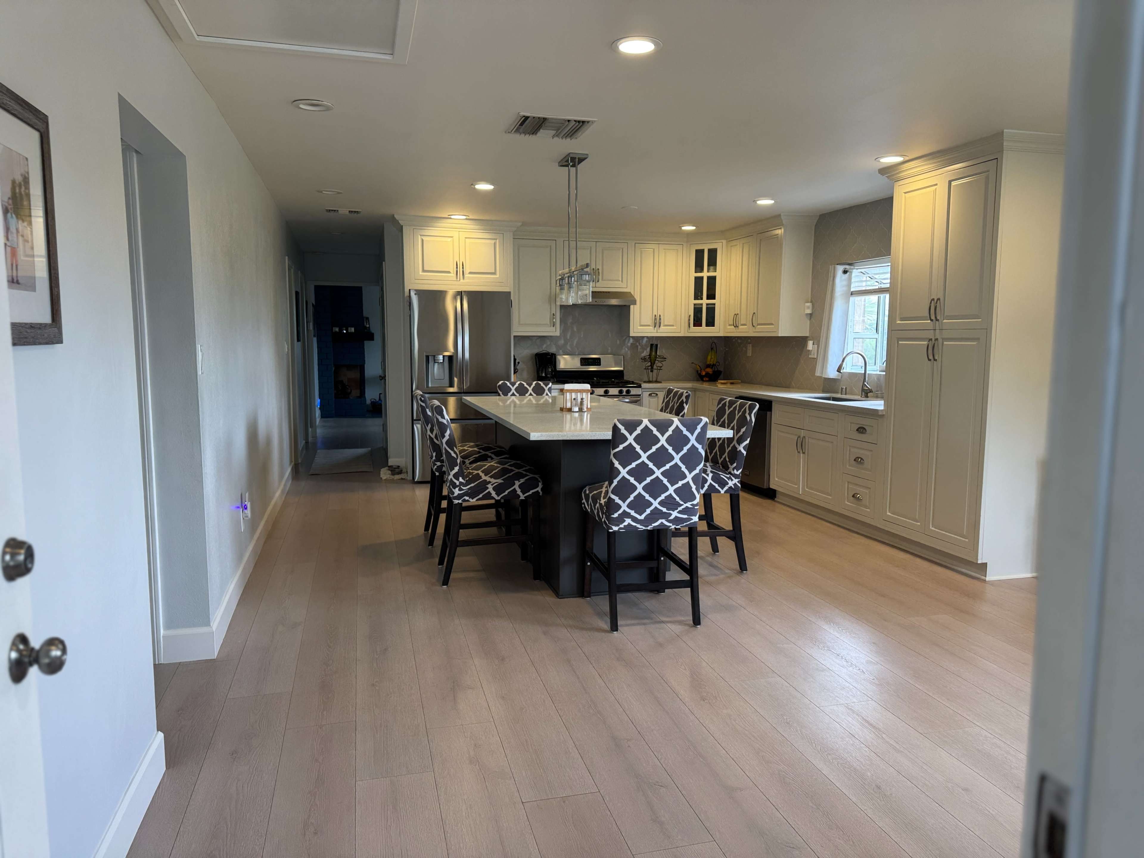 The image shows a modern kitchen with light-colored cabinetry, a large island, and a dining table surrounded by patterned chairs.