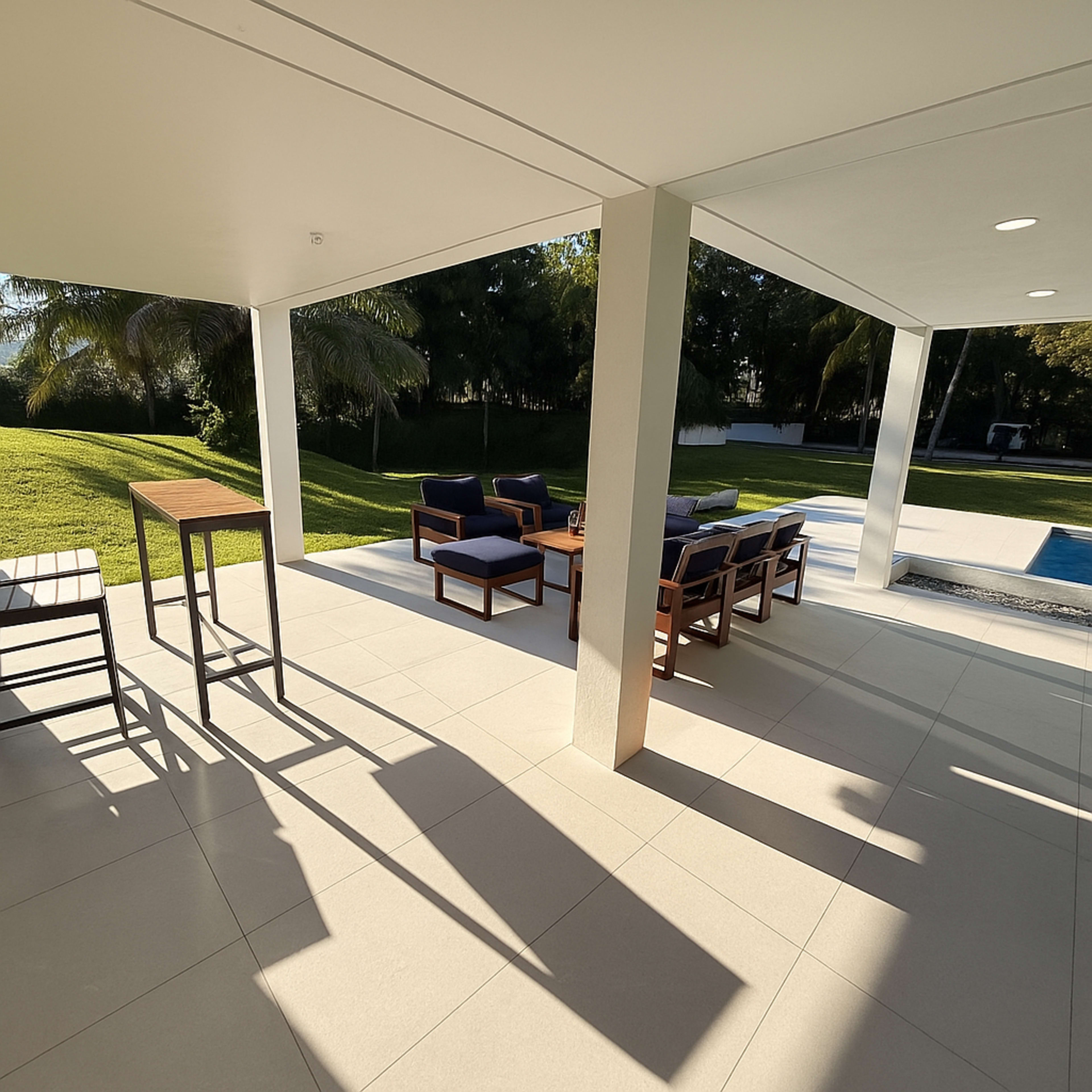 The image shows a patio area with outdoor seating, including chairs and a table, overlooking a grassy yard and a swimming pool.