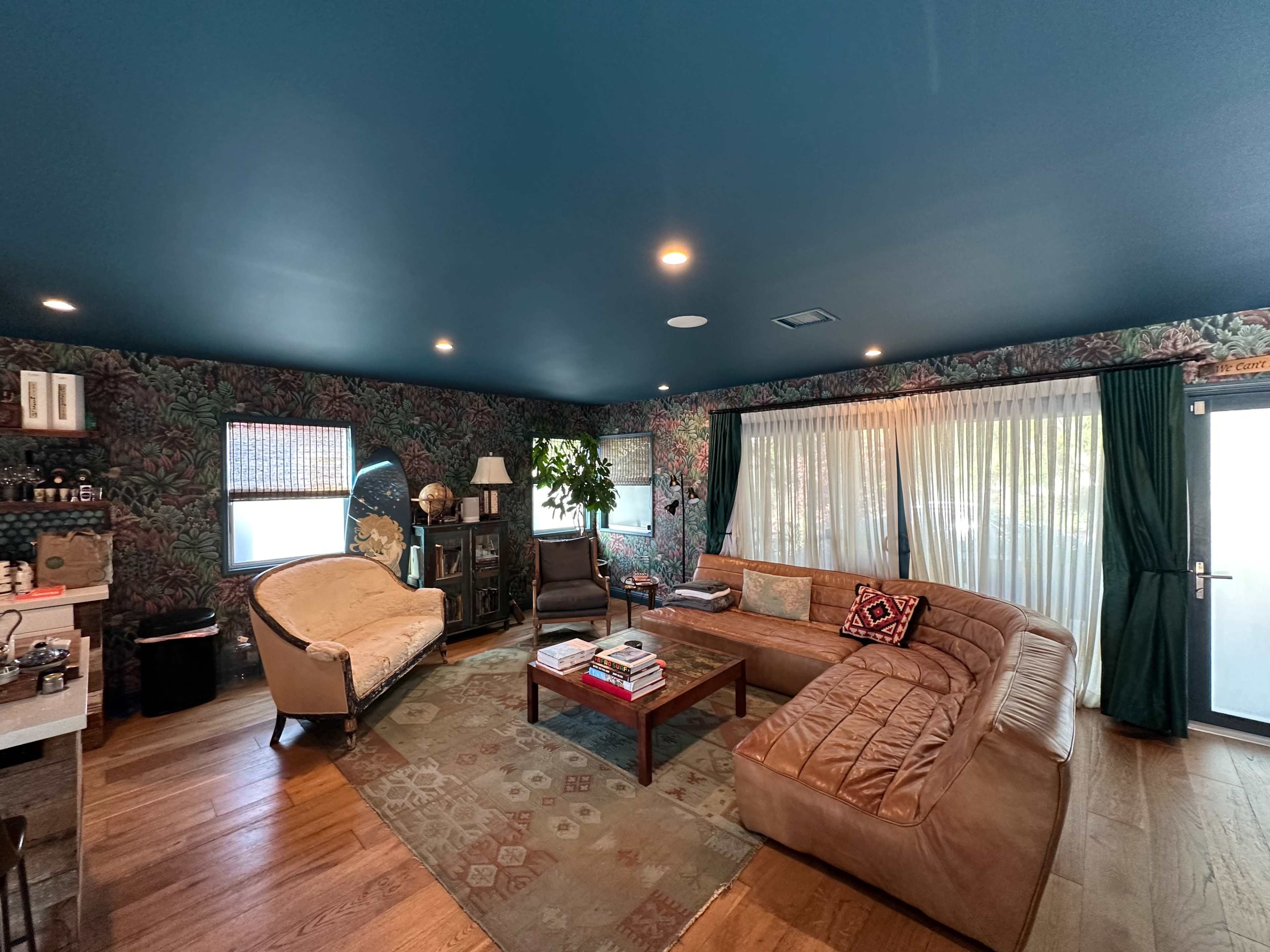 A living room with a brown sectional sofa, a small wooden coffee table, and patterned wallpaper featuring tropical foliage.