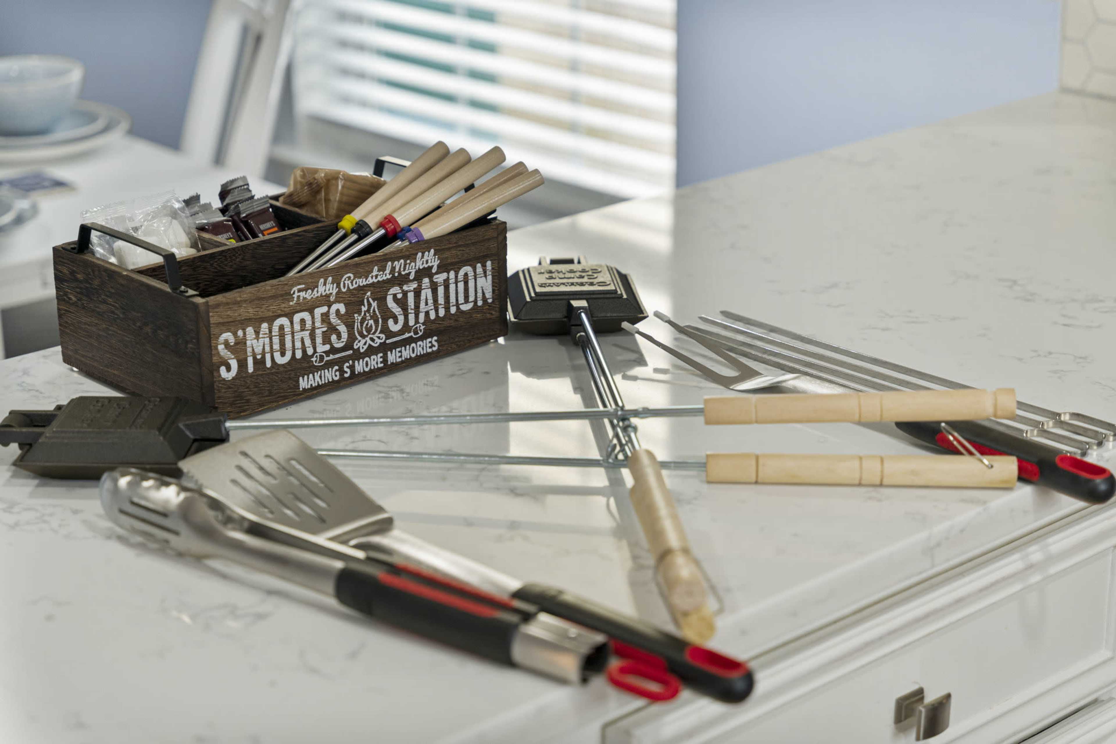 A wooden box labeled "S'mores Station" holds various utensils and tools for making s'mores on a countertop.