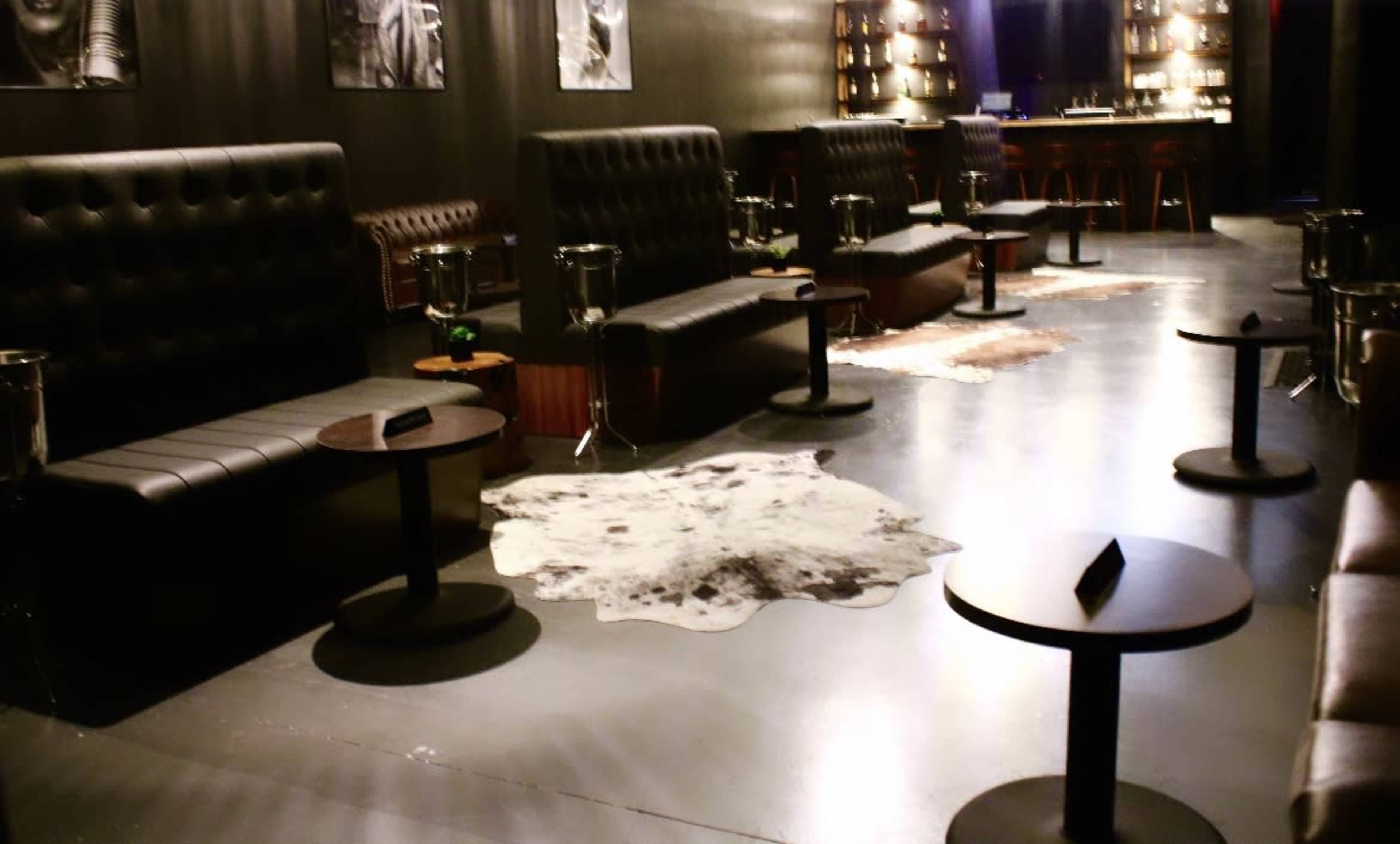 A dimly lit lounge with leather seating, low tables, and animal hide rugs on a polished floor.