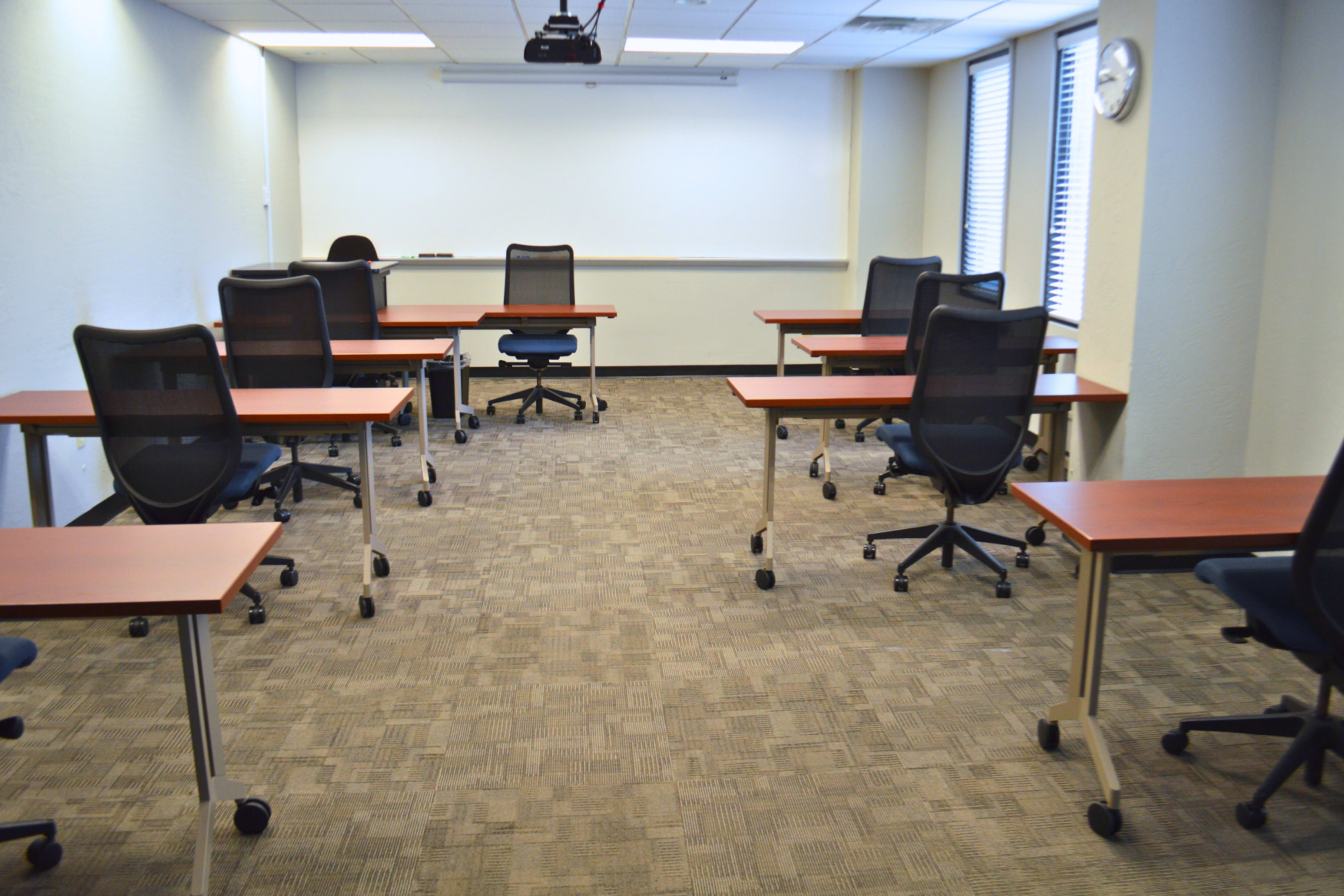 A conference room is arranged with several rolling chairs and desks, facing a blank whiteboard.