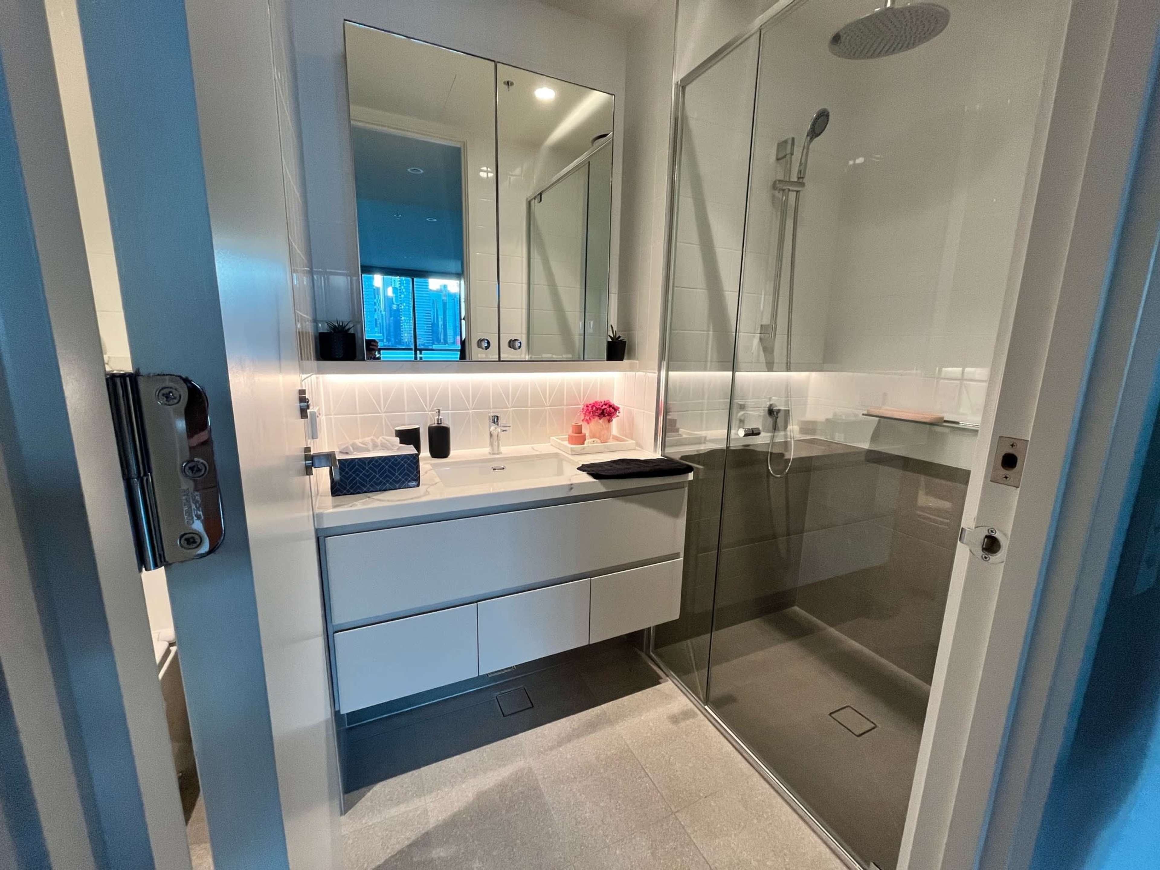 A modern bathroom featuring a glass shower enclosure, a sleek vanity with drawers, and a large mirror above the sink.