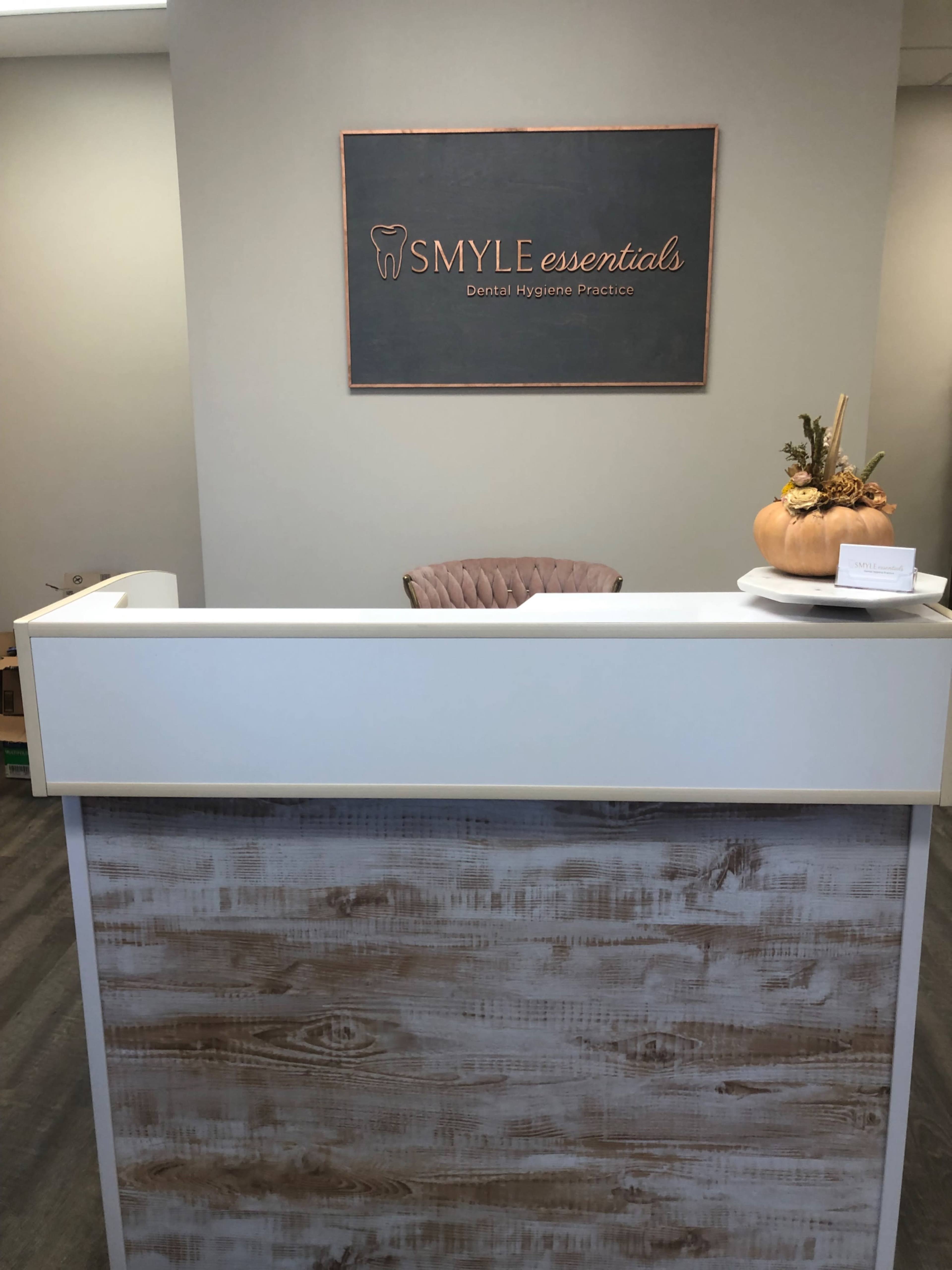 A dental practice reception desk with a sign that reads "SMYLE essentials" and a decorative pumpkin on the counter.