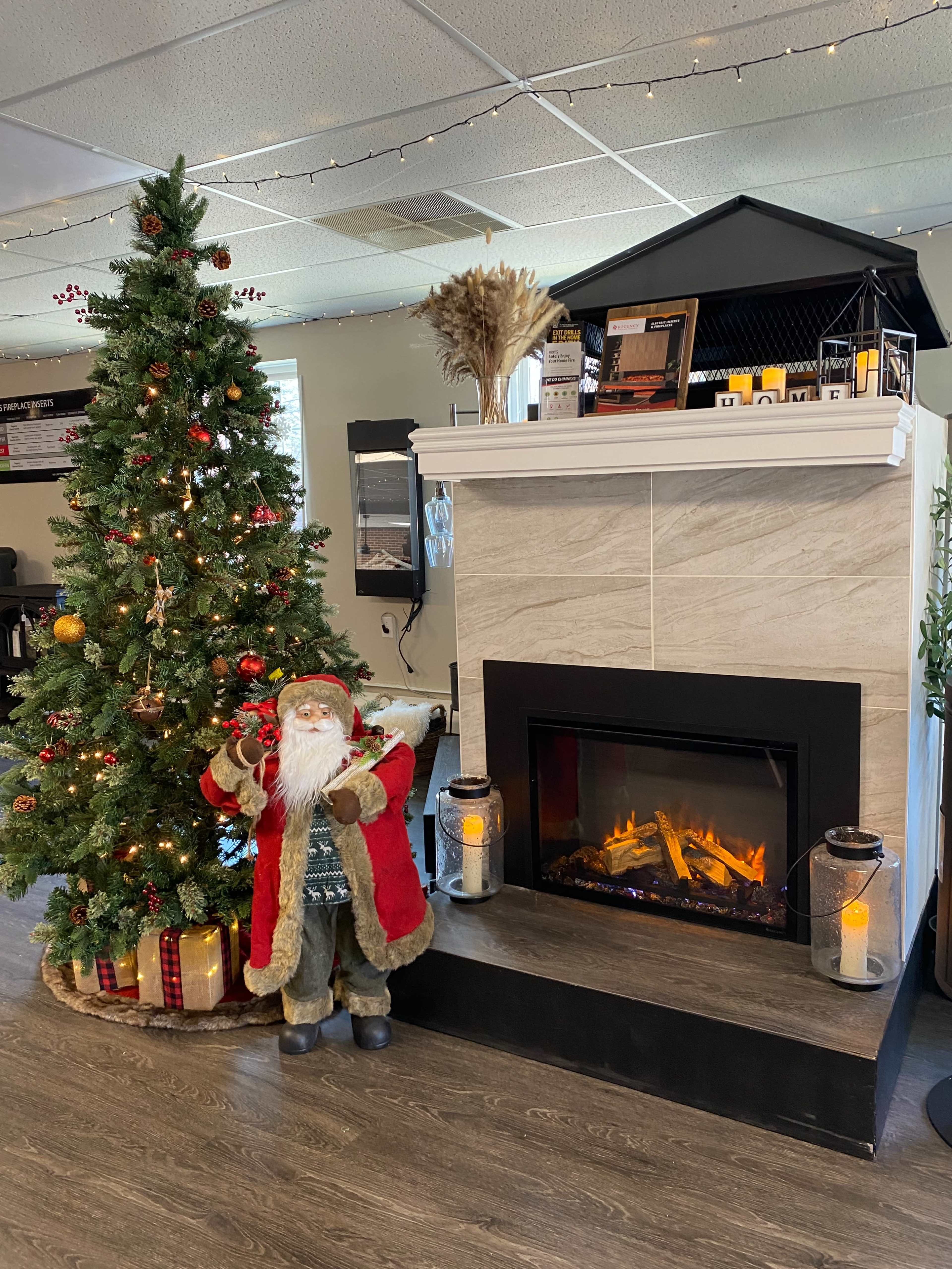 A decorated Christmas tree next to a fireplace with a Santa Claus figure standing in front.