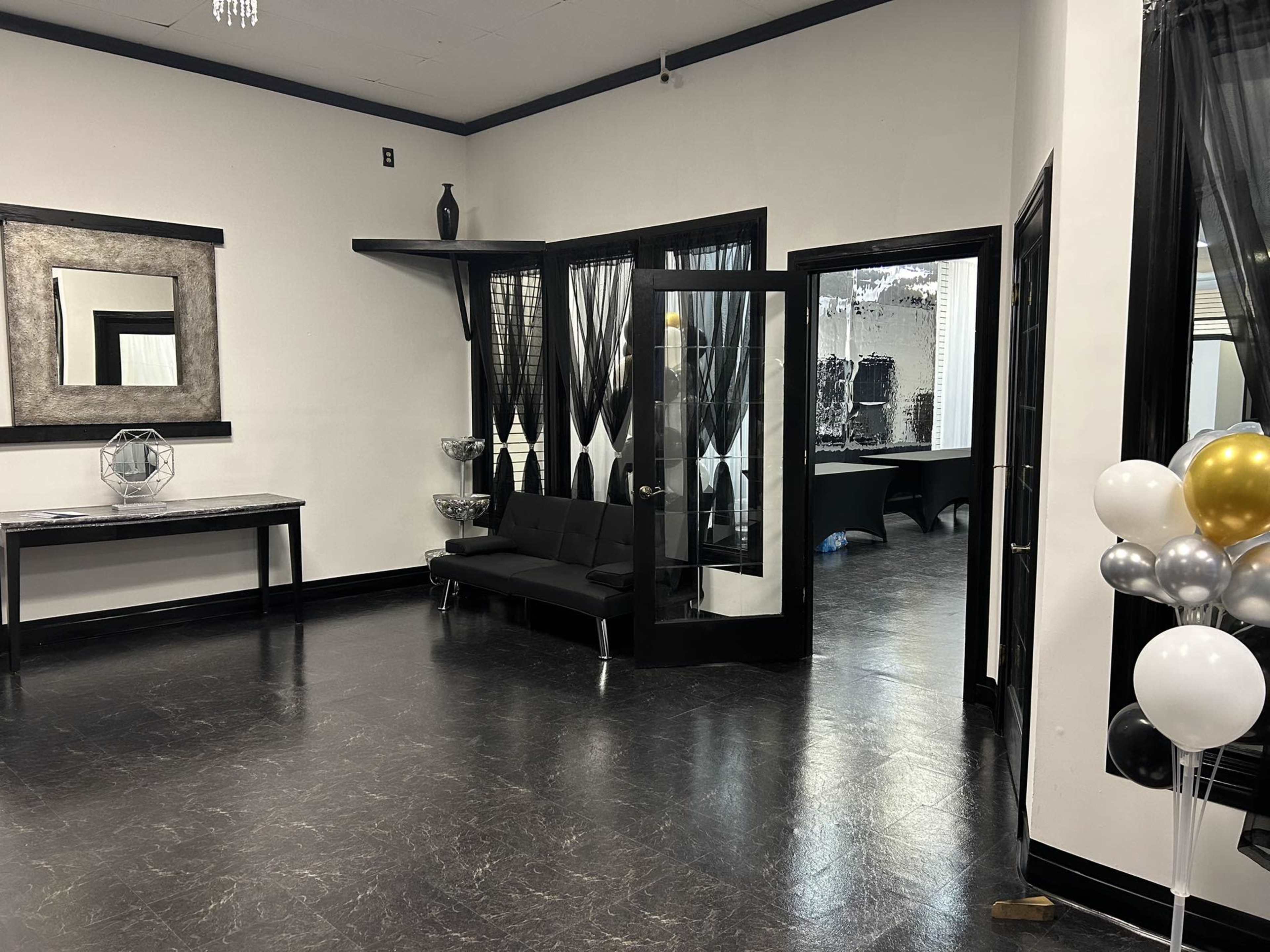 A spacious interior with black and white decor, featuring a black couch and a mirrored wall, along with a doorway leading to another room.
