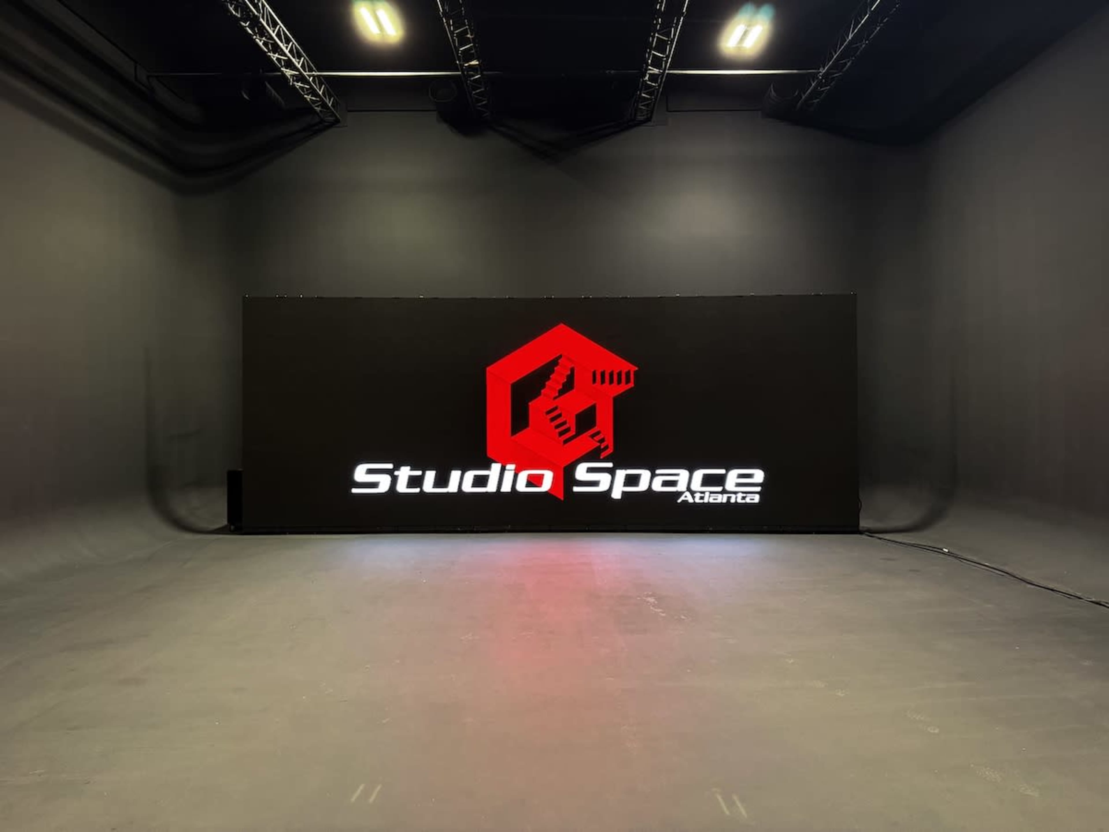 The image shows a large, dark studio space with a prominent illuminated sign displaying "Studio Space Atlanta" against a plain backdrop.
