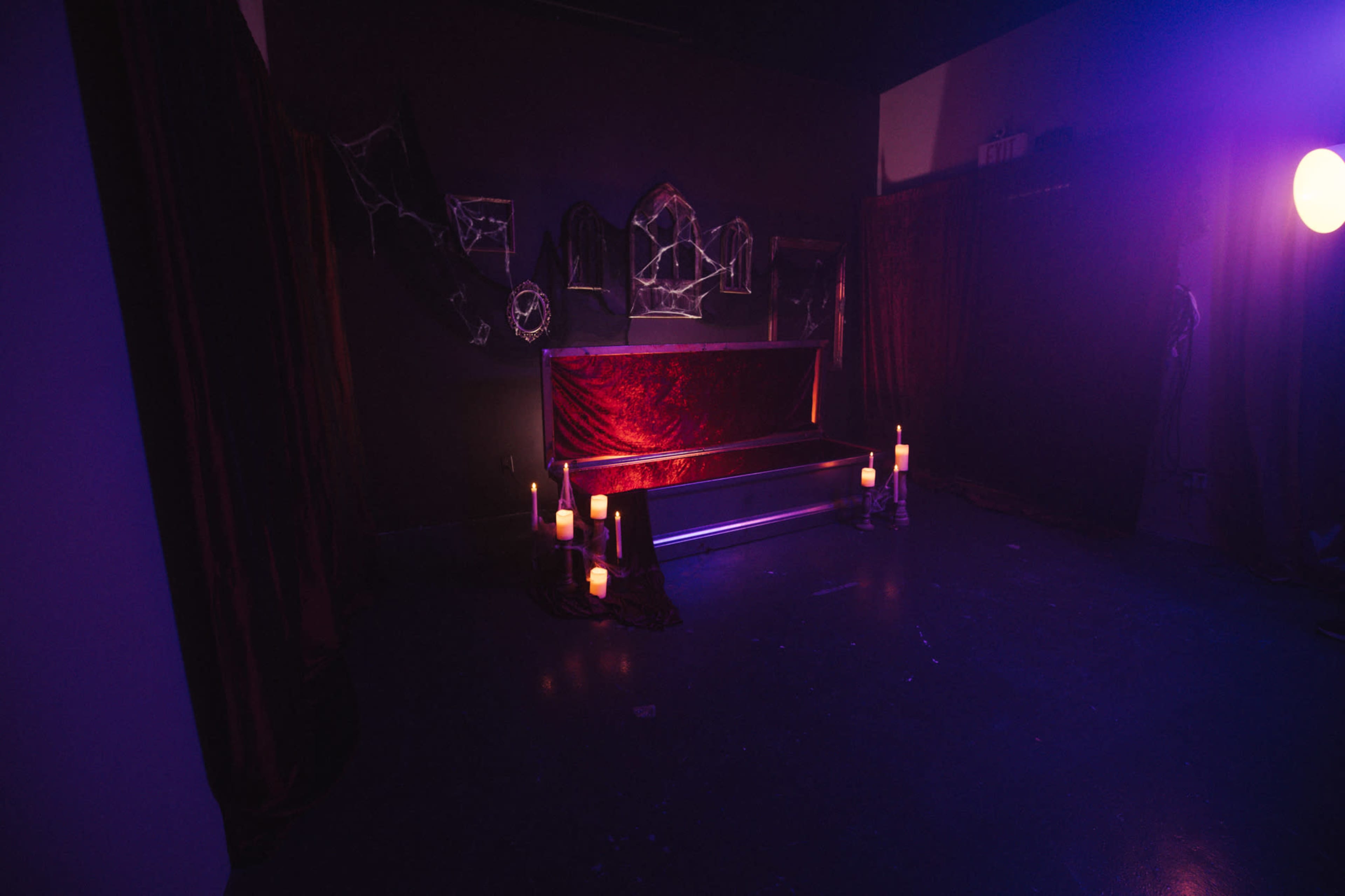 The scene depicts a dimly lit room with a red velvet bench, dark drapes, cobwebs on the walls, and candles arranged nearby.