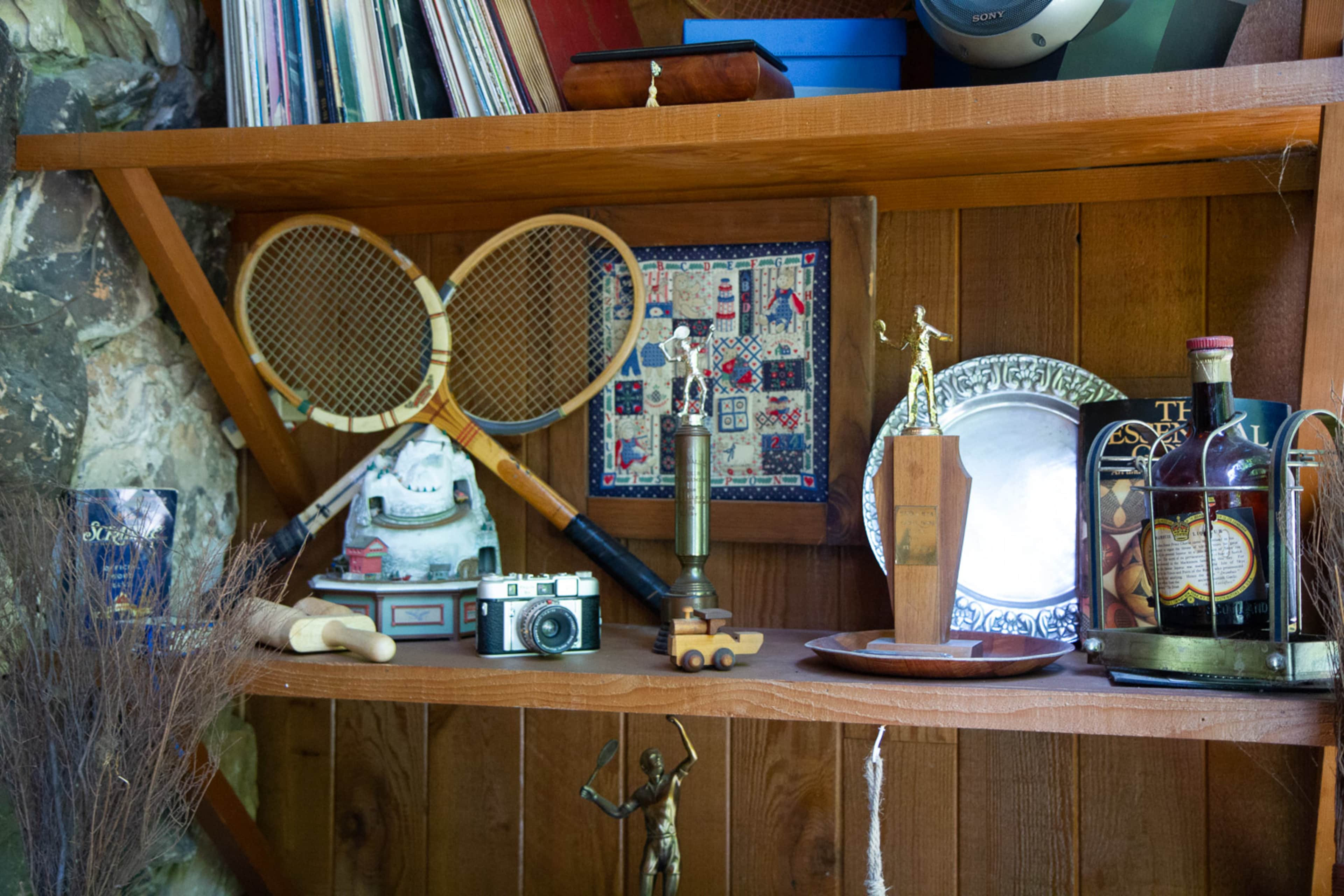 A wooden shelf displays various vintage items including two tennis rackets, a camera, a decorative plate, and a small trophy.