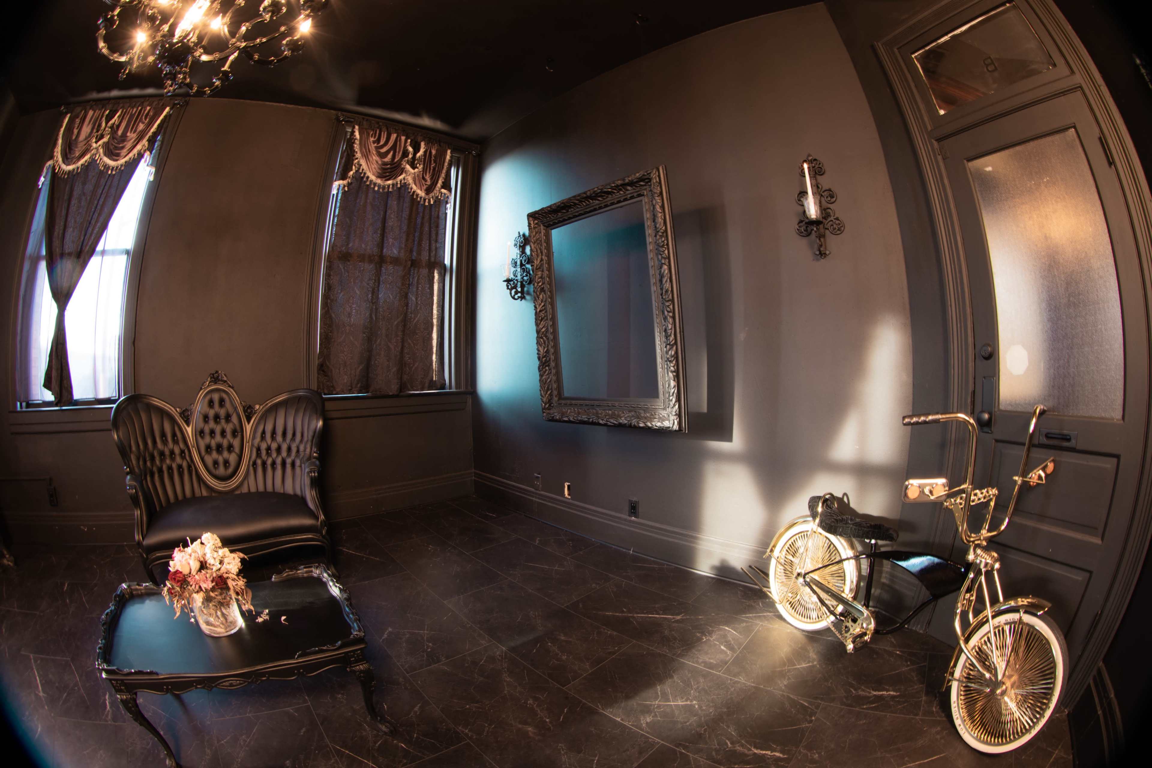The image showcases a stylishly decorated room featuring a black ornate mirror and a vintage bicycle beside an elegant chair and table with flowers.
